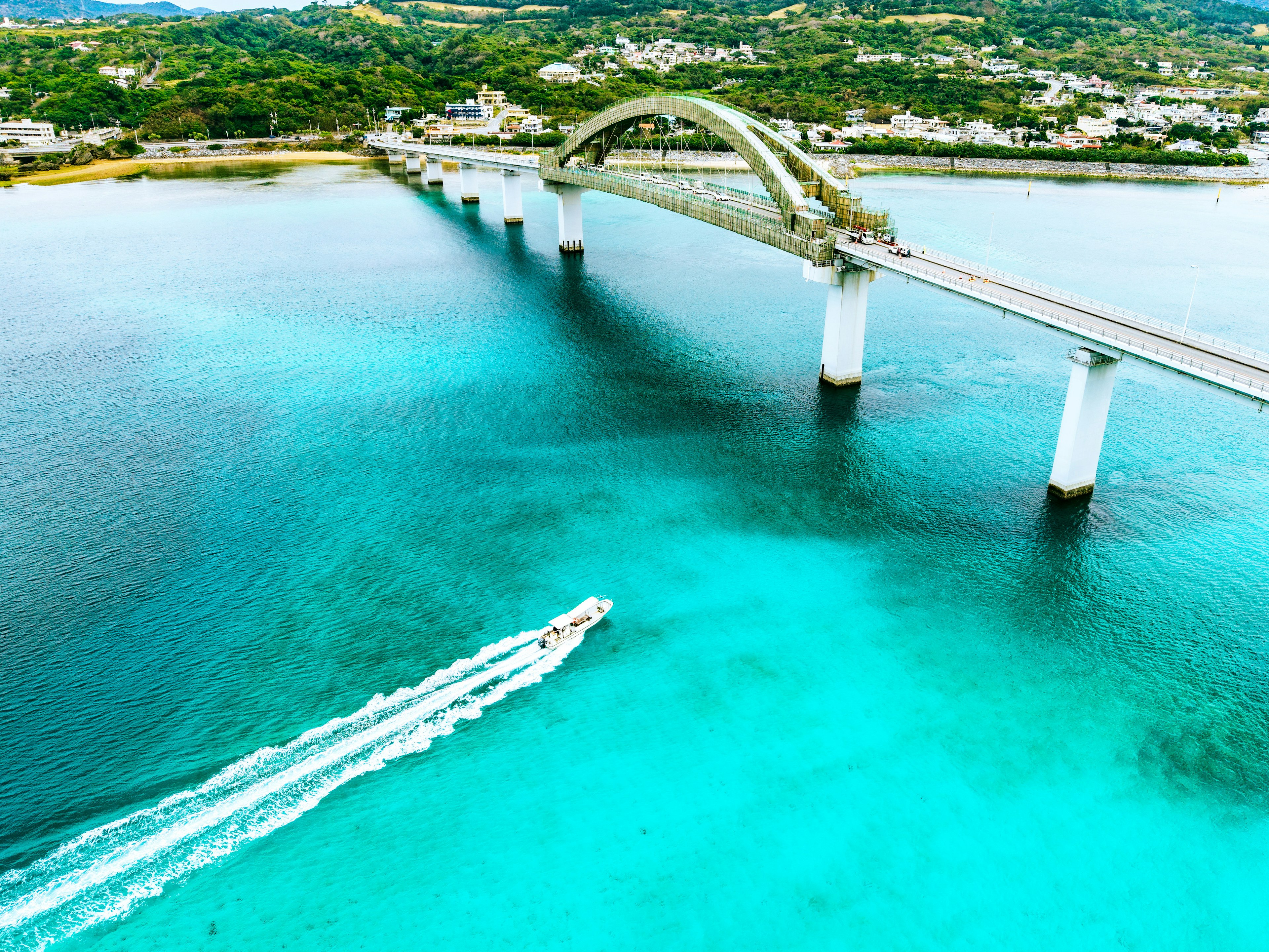 Vista aerea di un mare turchese con un ponte e una barca che passa