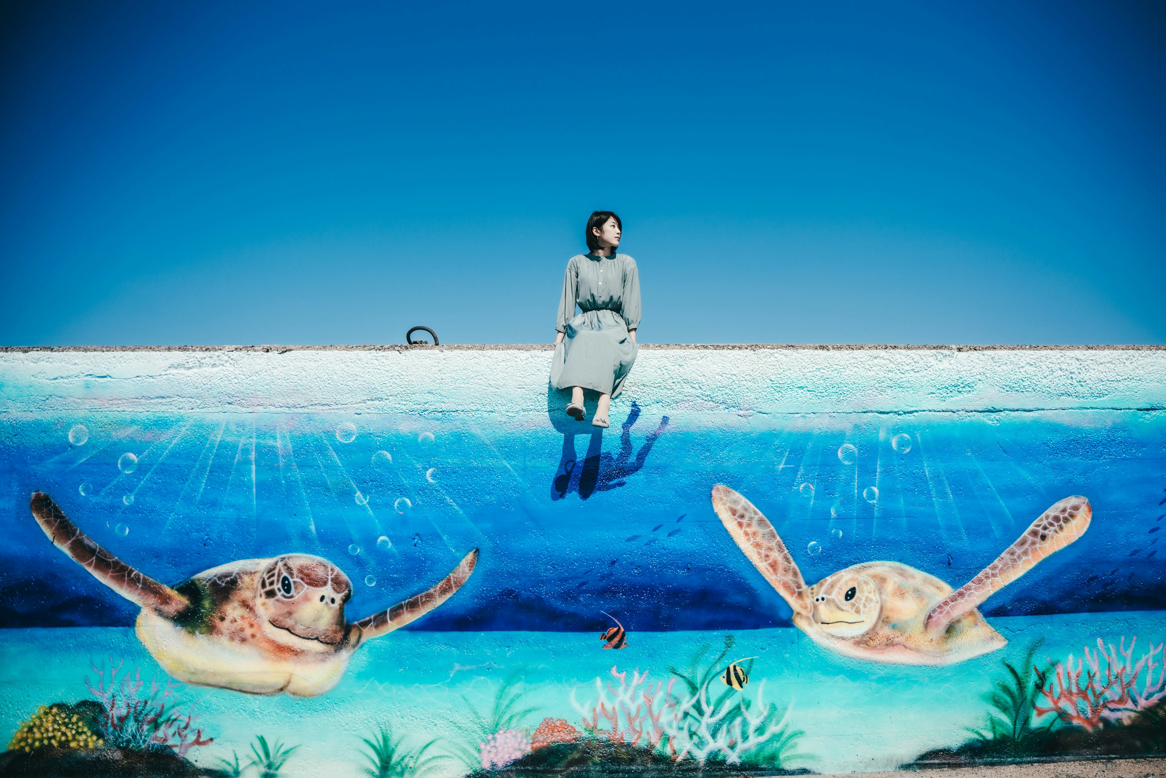 Une femme se tenant devant une fresque murale bleue représentant deux tortues