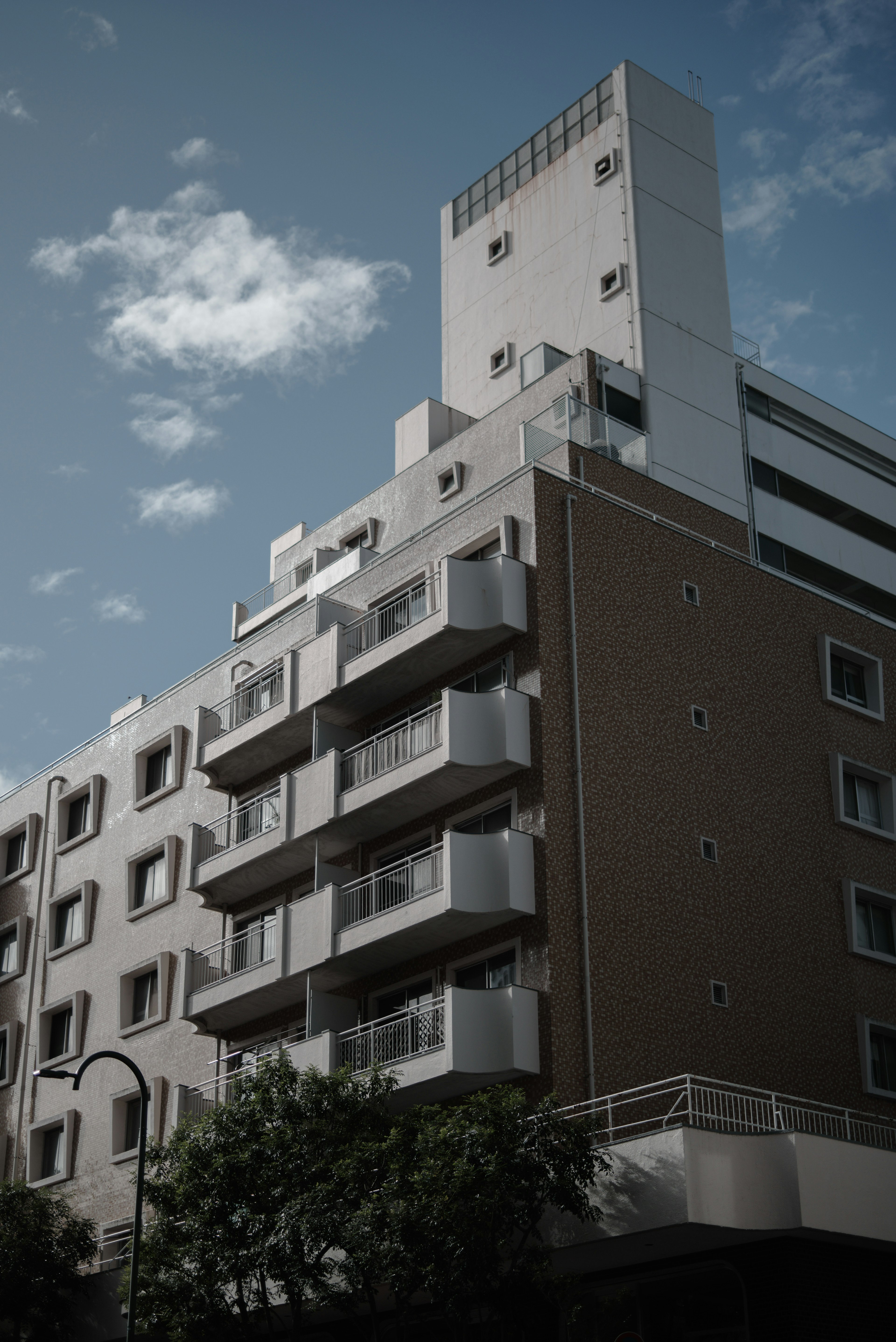 Modern building with balconies, contrasting white and brown facade, under a cloudy blue sky