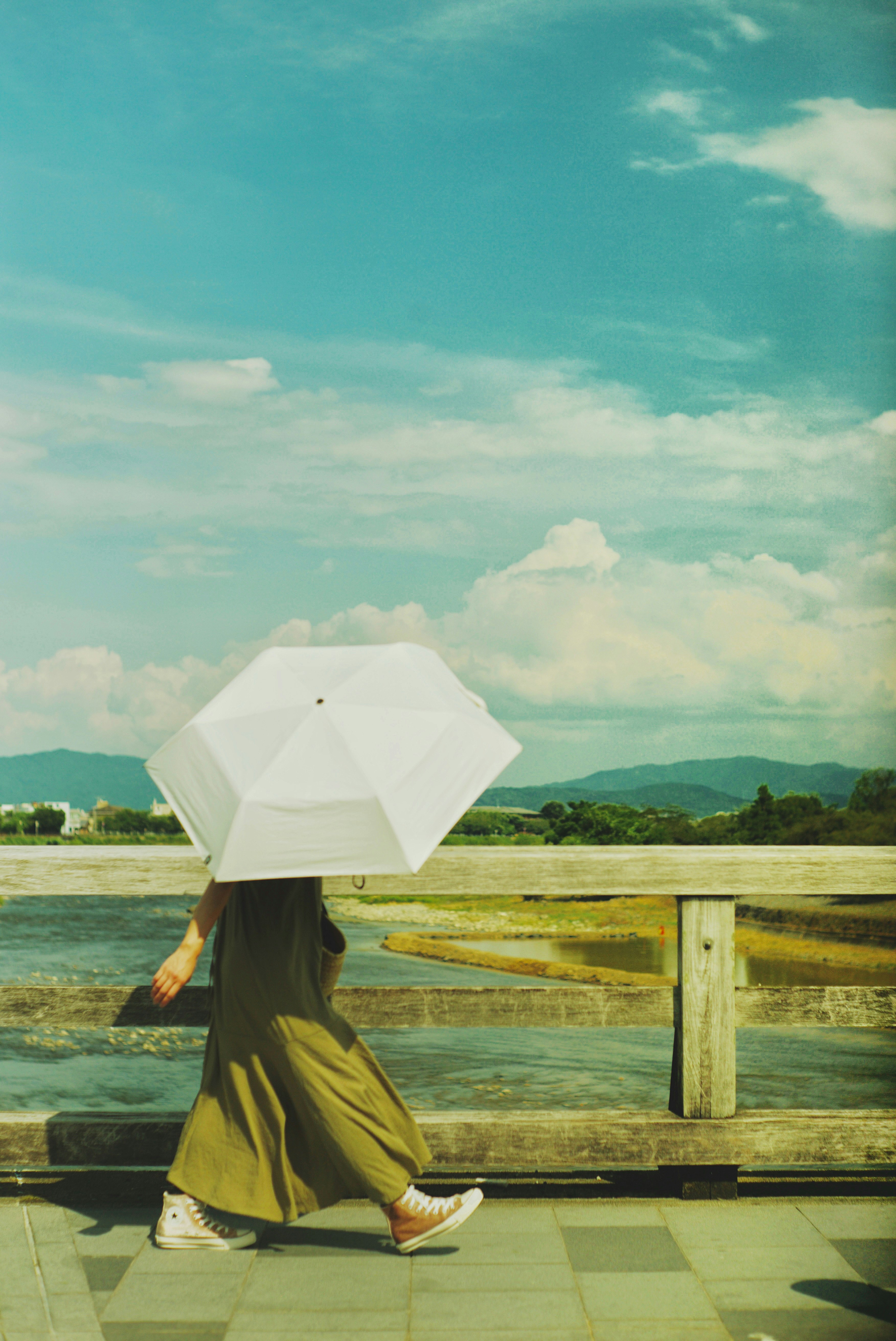 A woman walking with a white umbrella under a blue sky