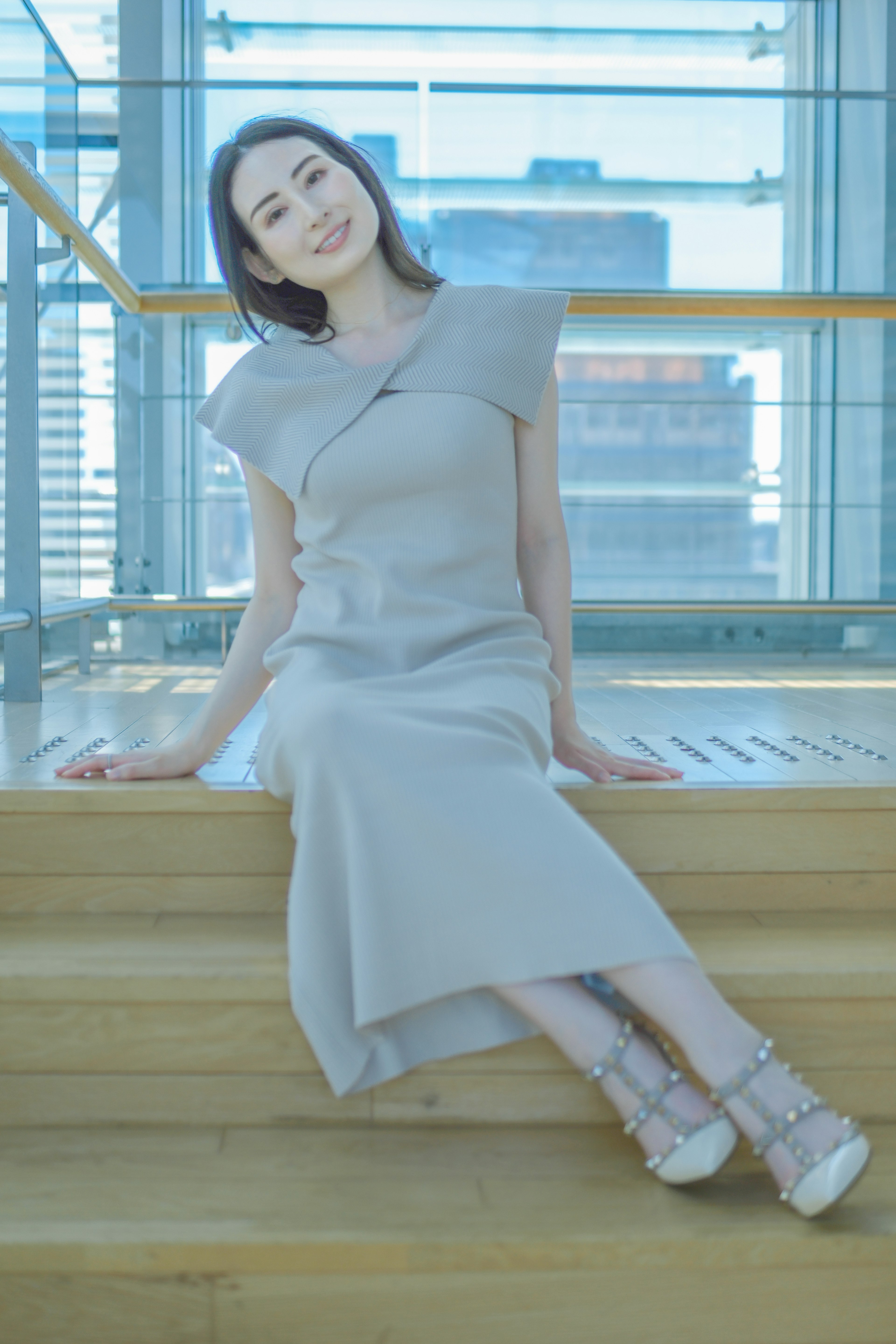 A woman in a stylish gray dress sitting on wooden stairs smiling