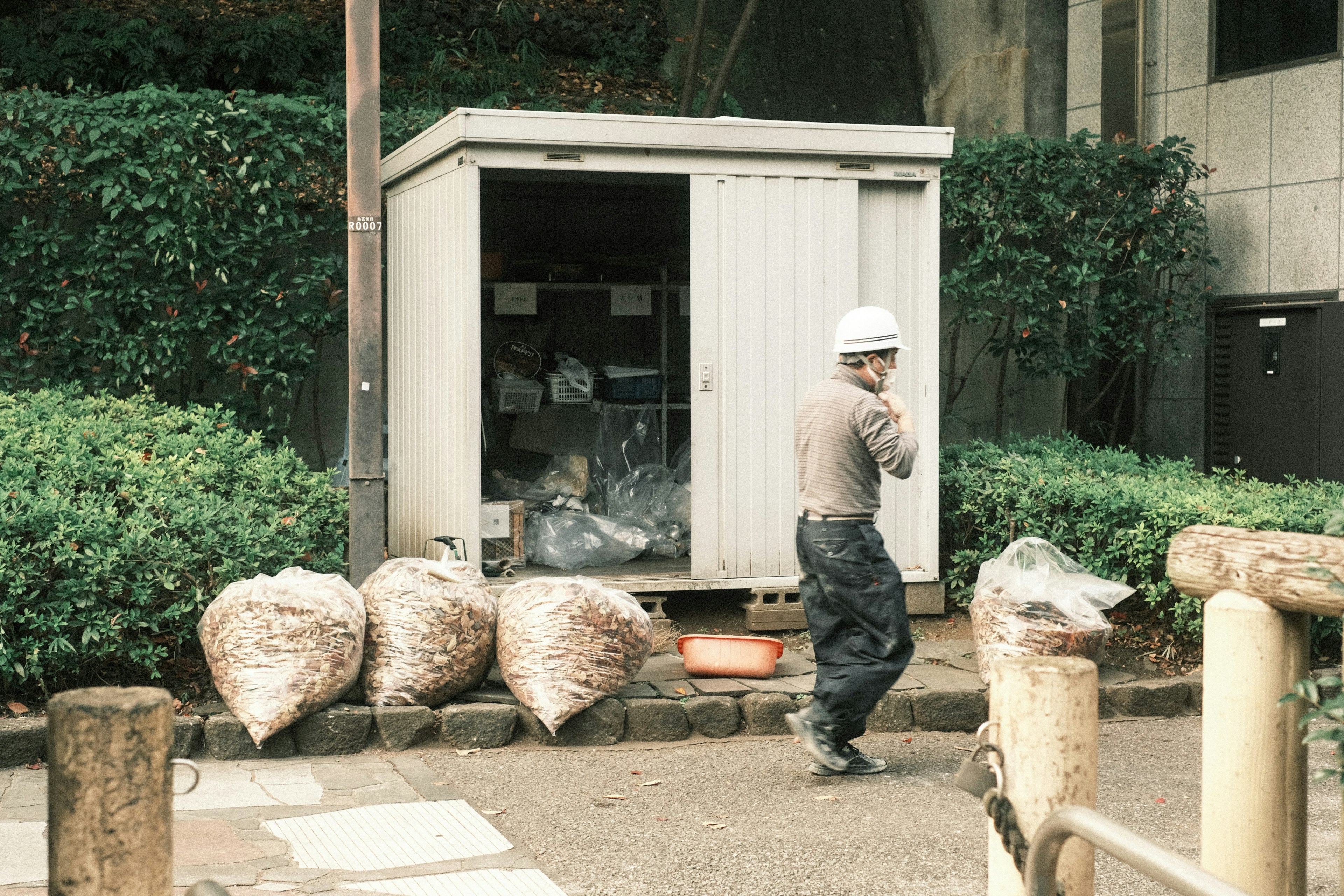 A worker in a uniform carrying trash near a storage shed