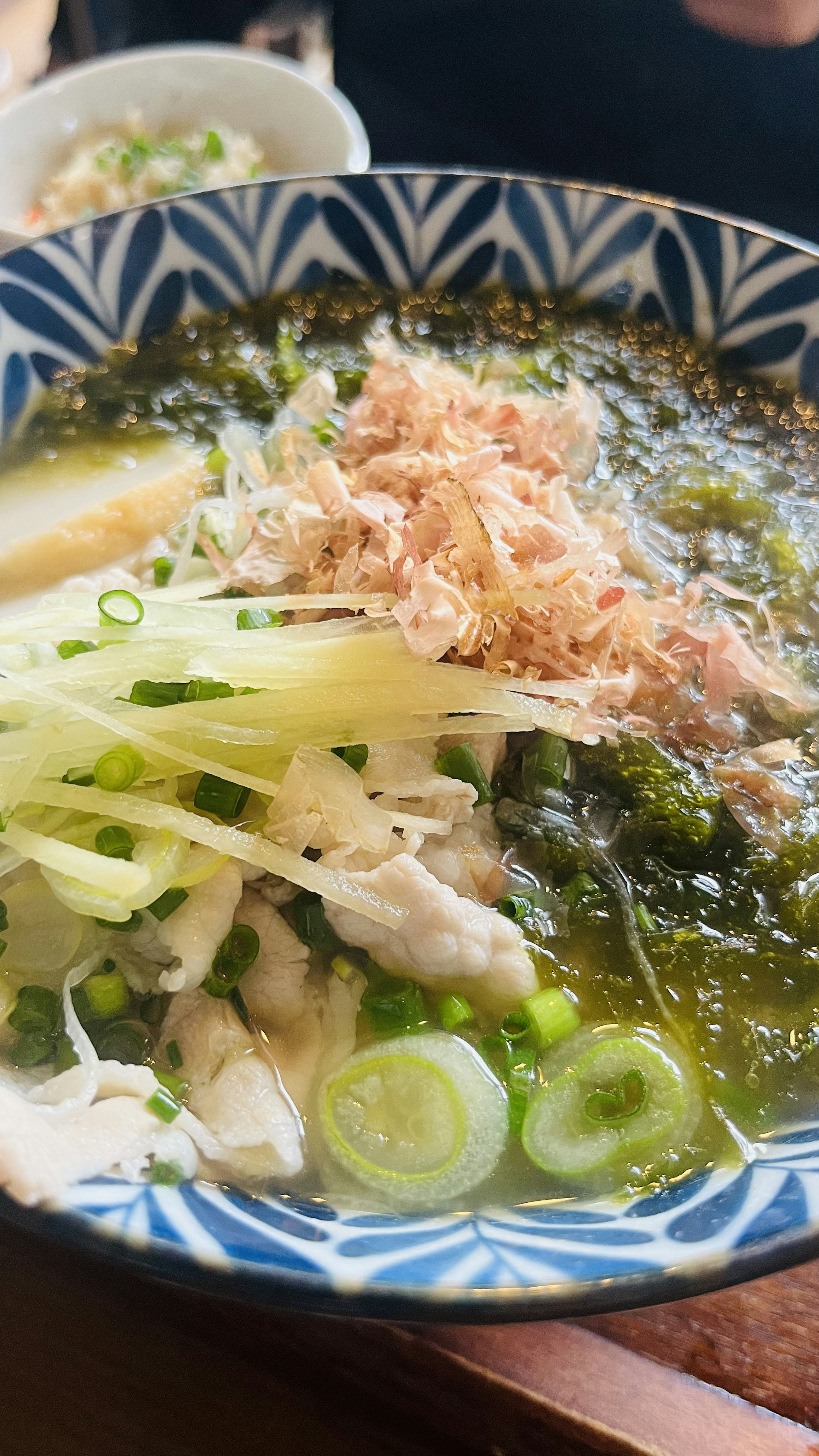 A bowl of green soup topped with shredded green onions and bonito flakes