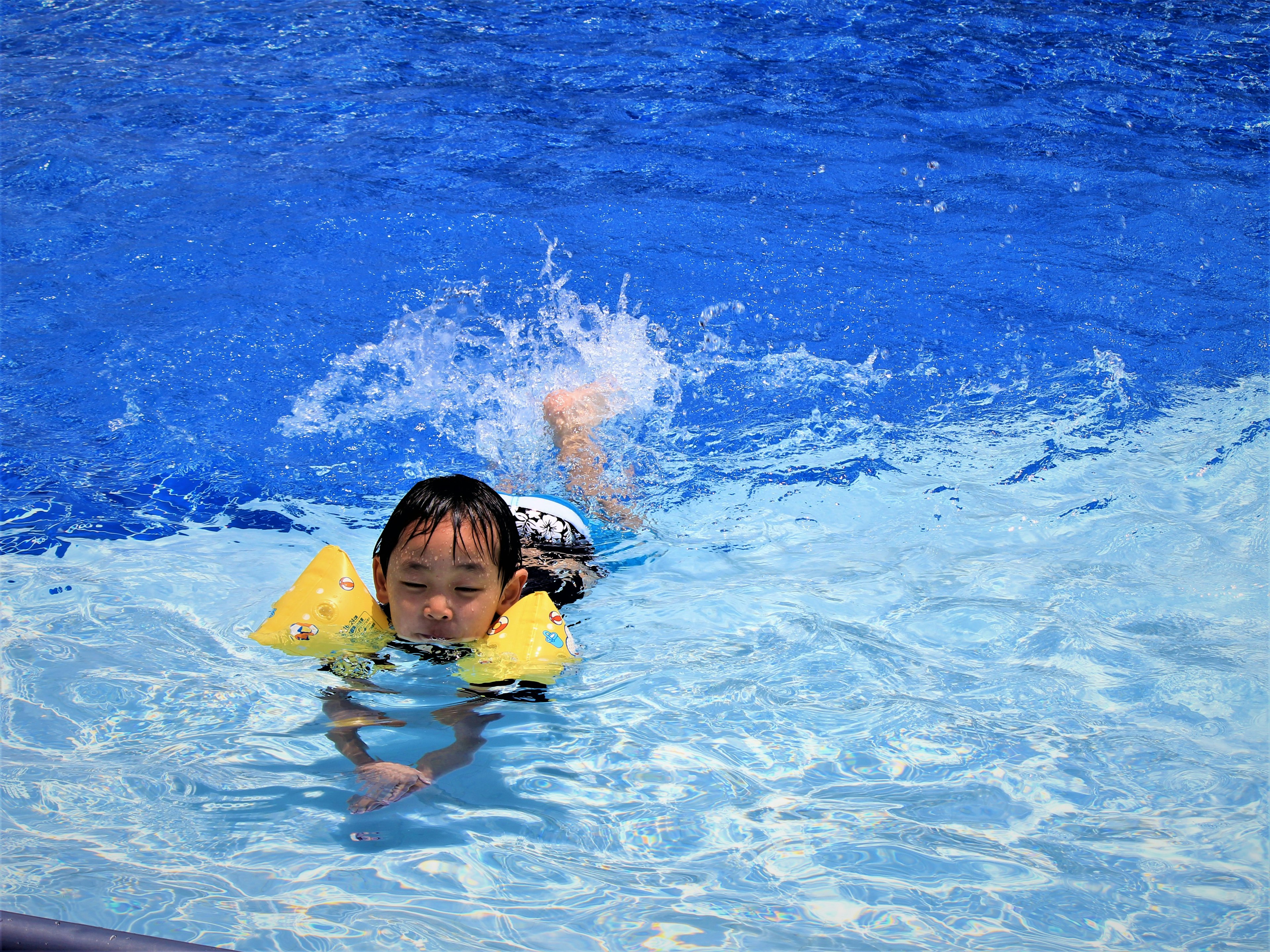 Bambino che nuota in piscina con braccioli gialli