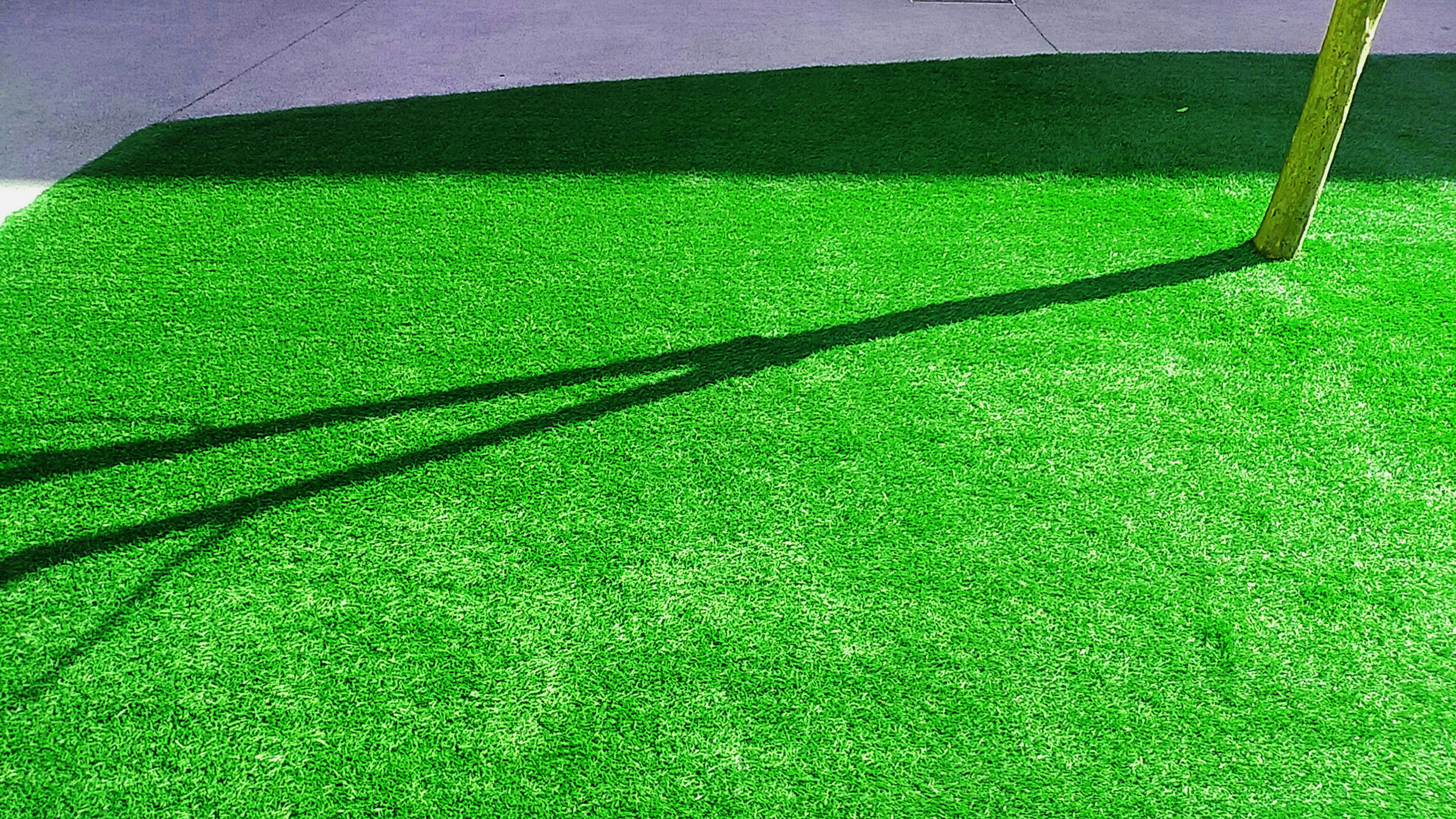 A vibrant green artificial grass surface with a long shadow cast on it