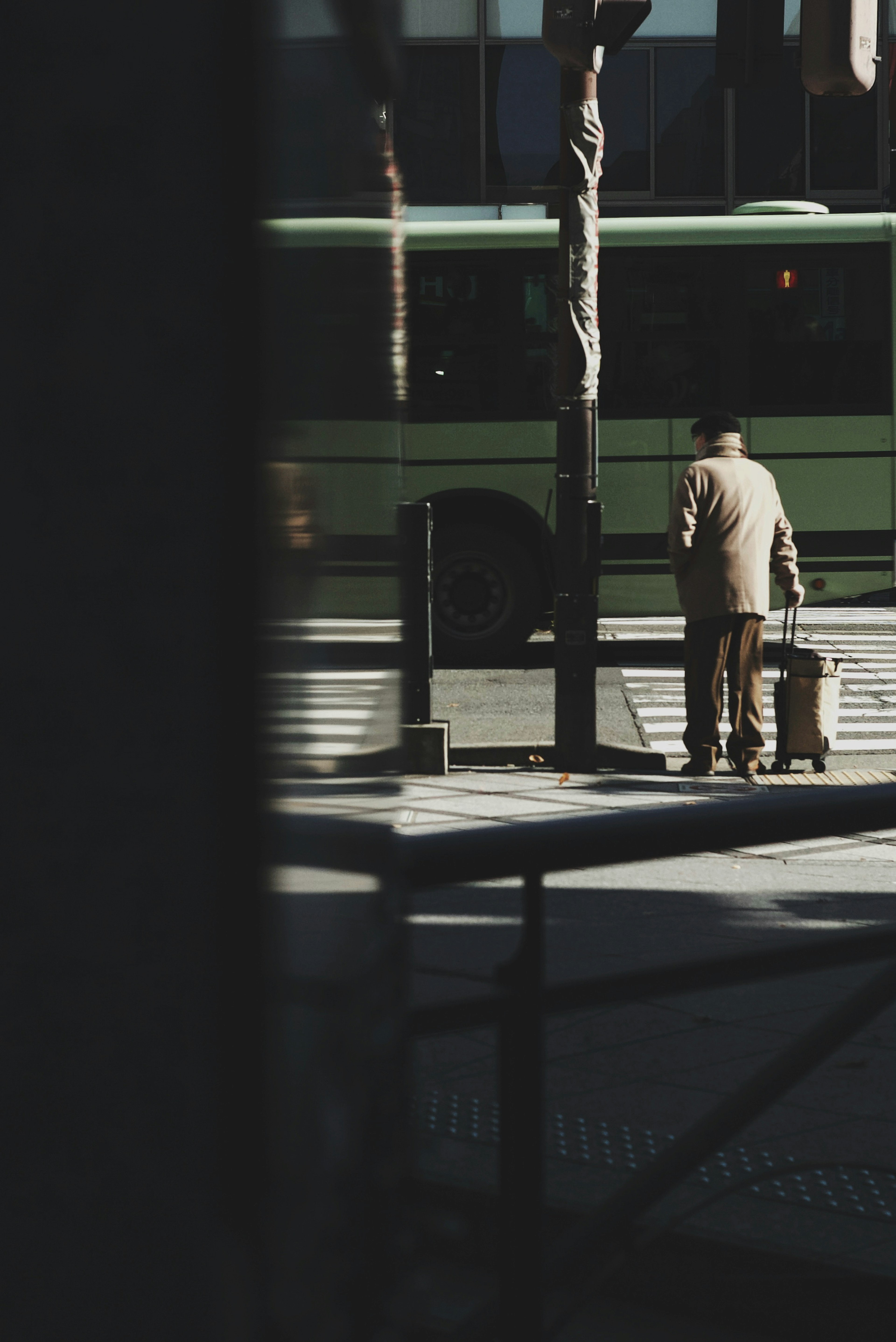 A man in a suit holding a suitcase with a green bus in the background on a city street