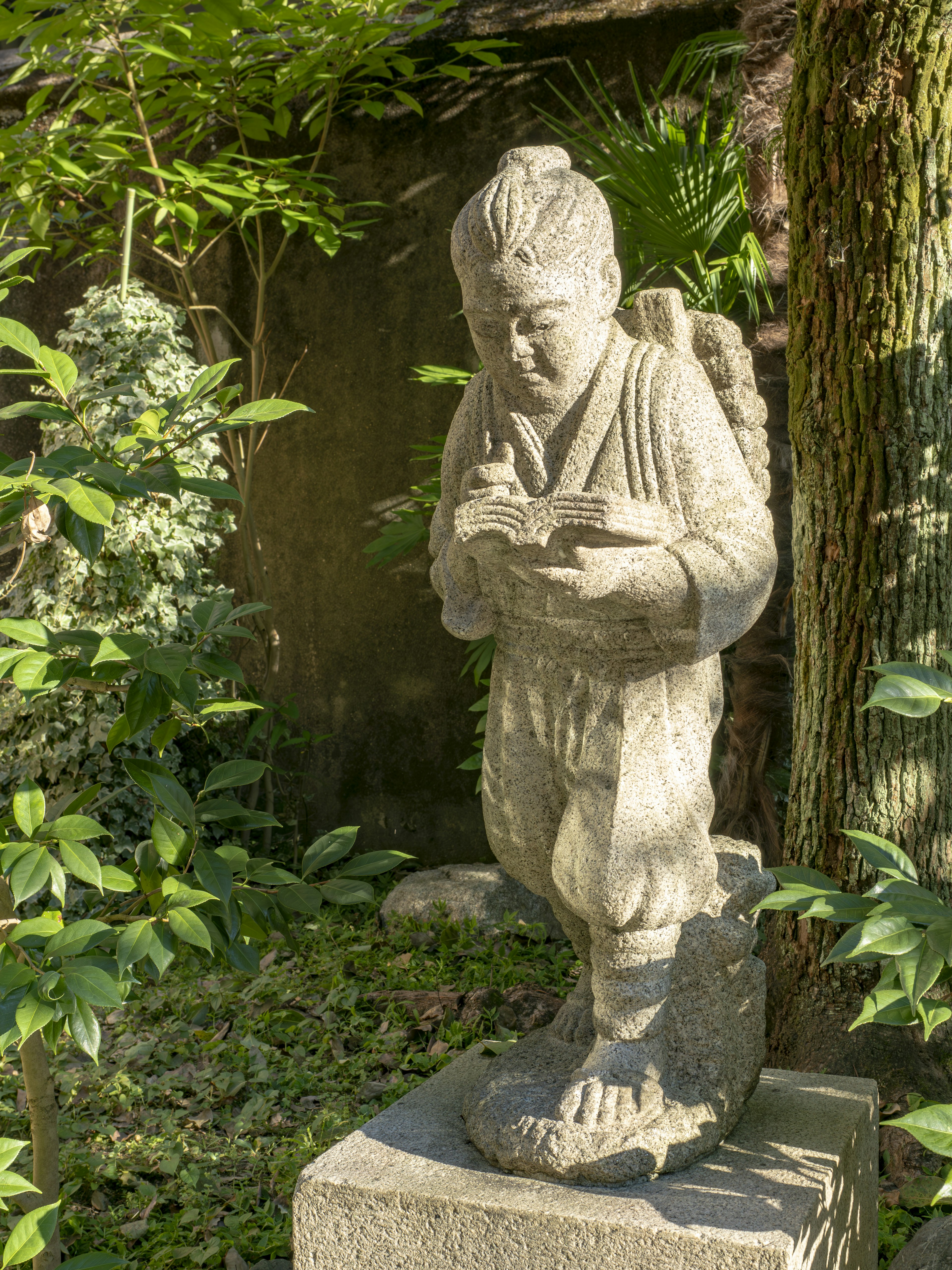 Estatua de piedra de un niño leyendo un libro en un jardín