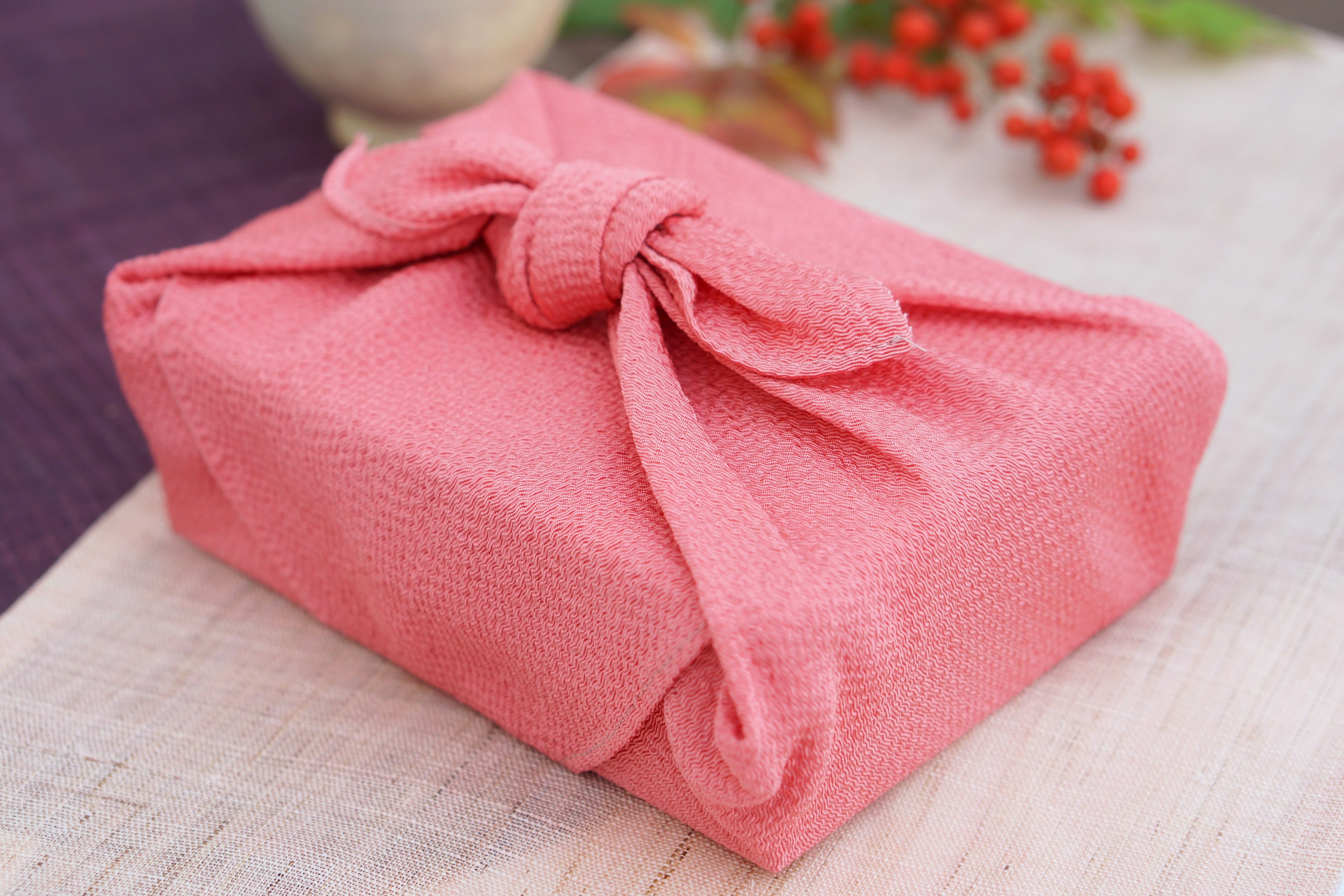 Boîte-cadeau enveloppée dans un tissu rose entourée de baies rouges et d'éléments naturels