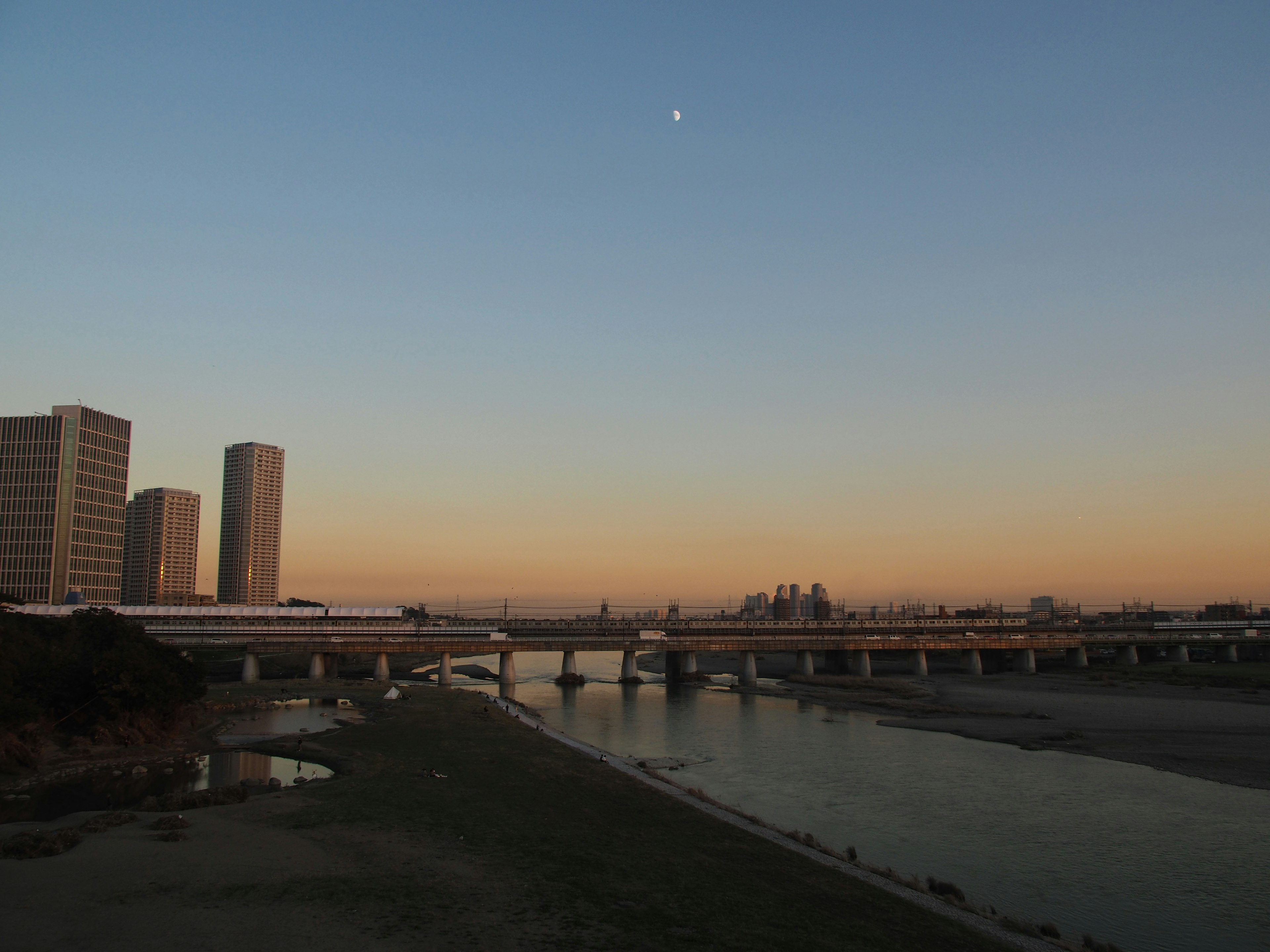 City skyline at dusk with a river and bridge in the foreground