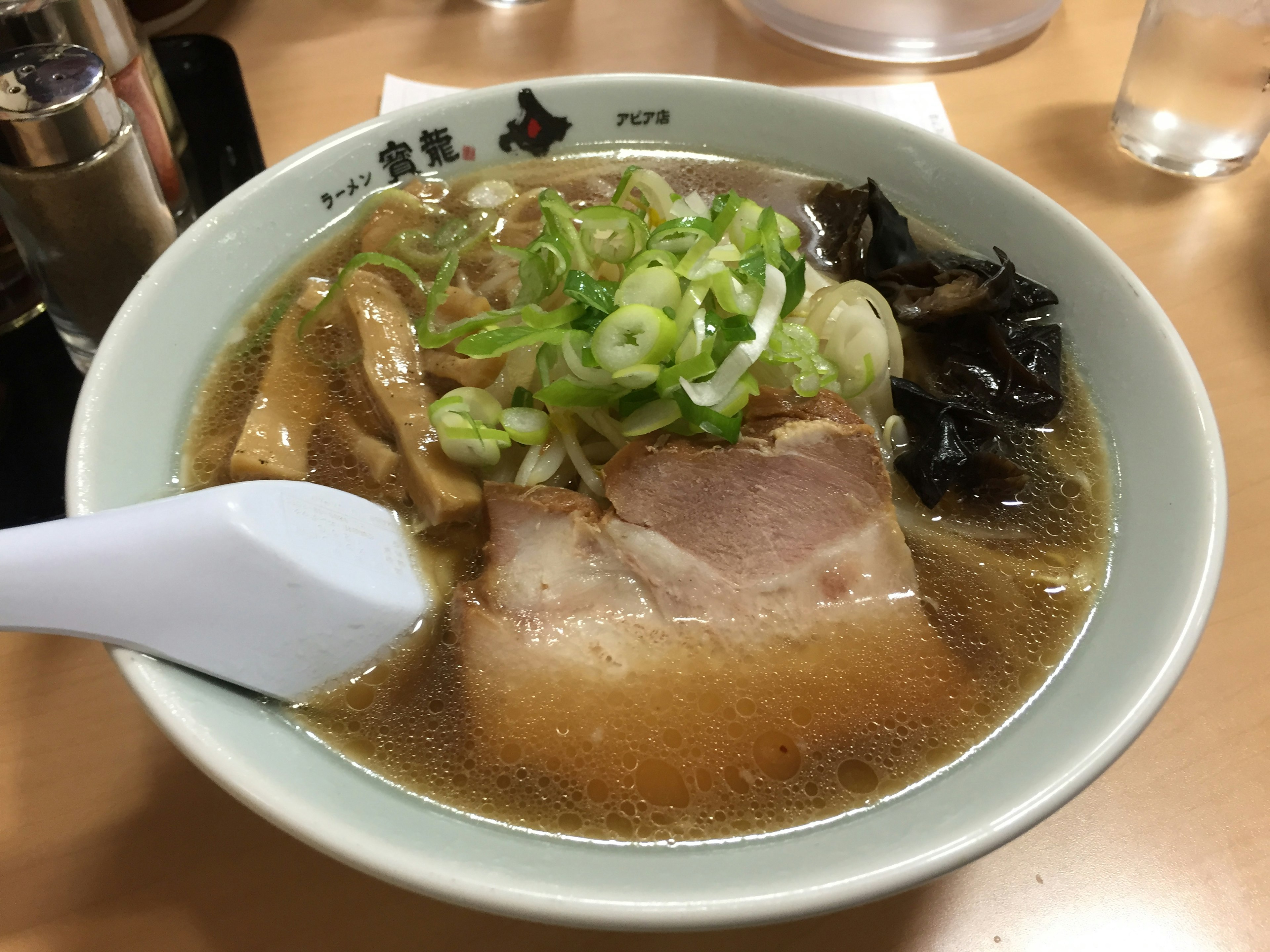 Tazón de ramen cubierto con chashu, cebollas verdes y hongos negros