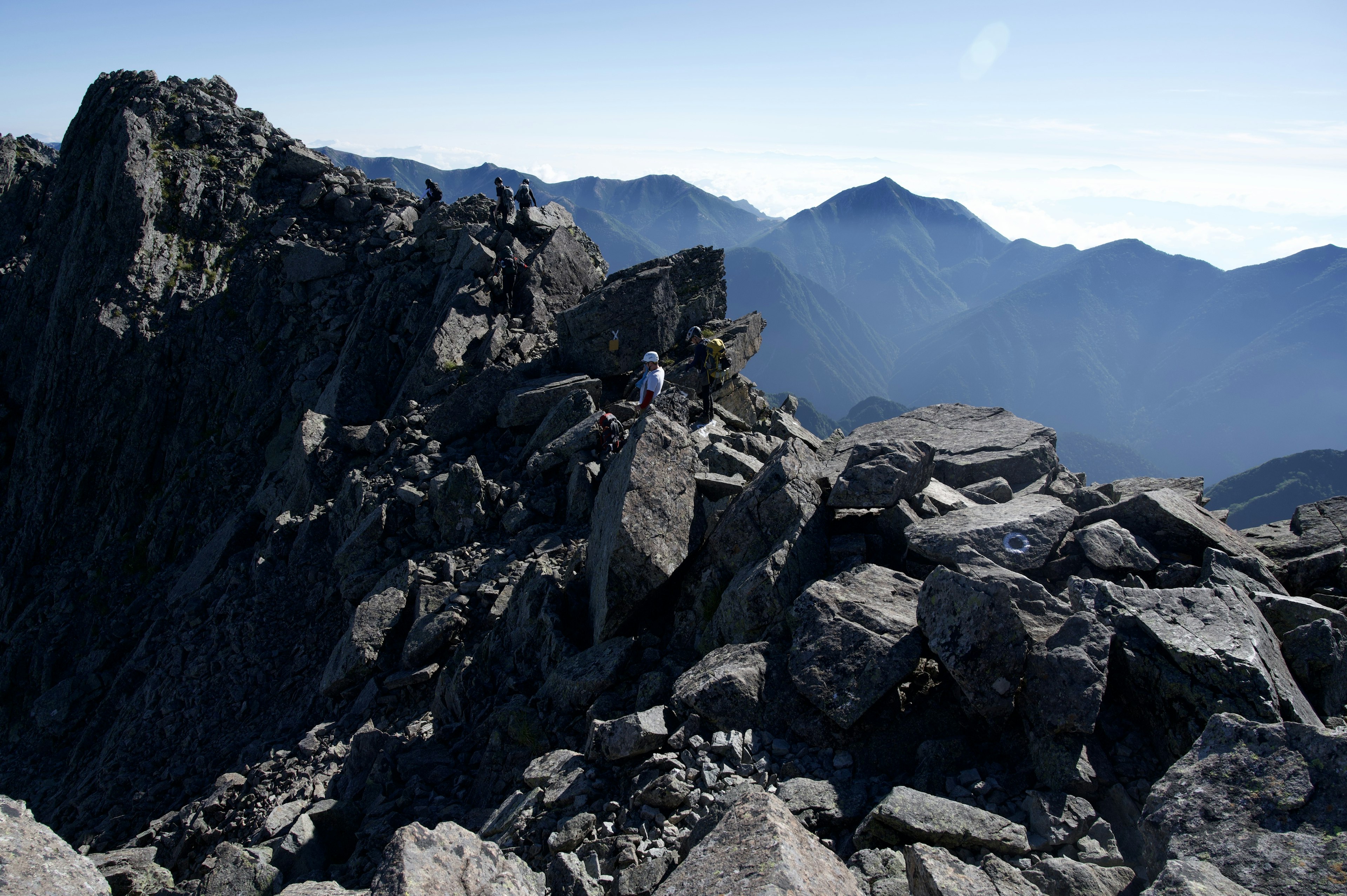 険しい山の頂上に立つ登山者の姿と遠くの山々