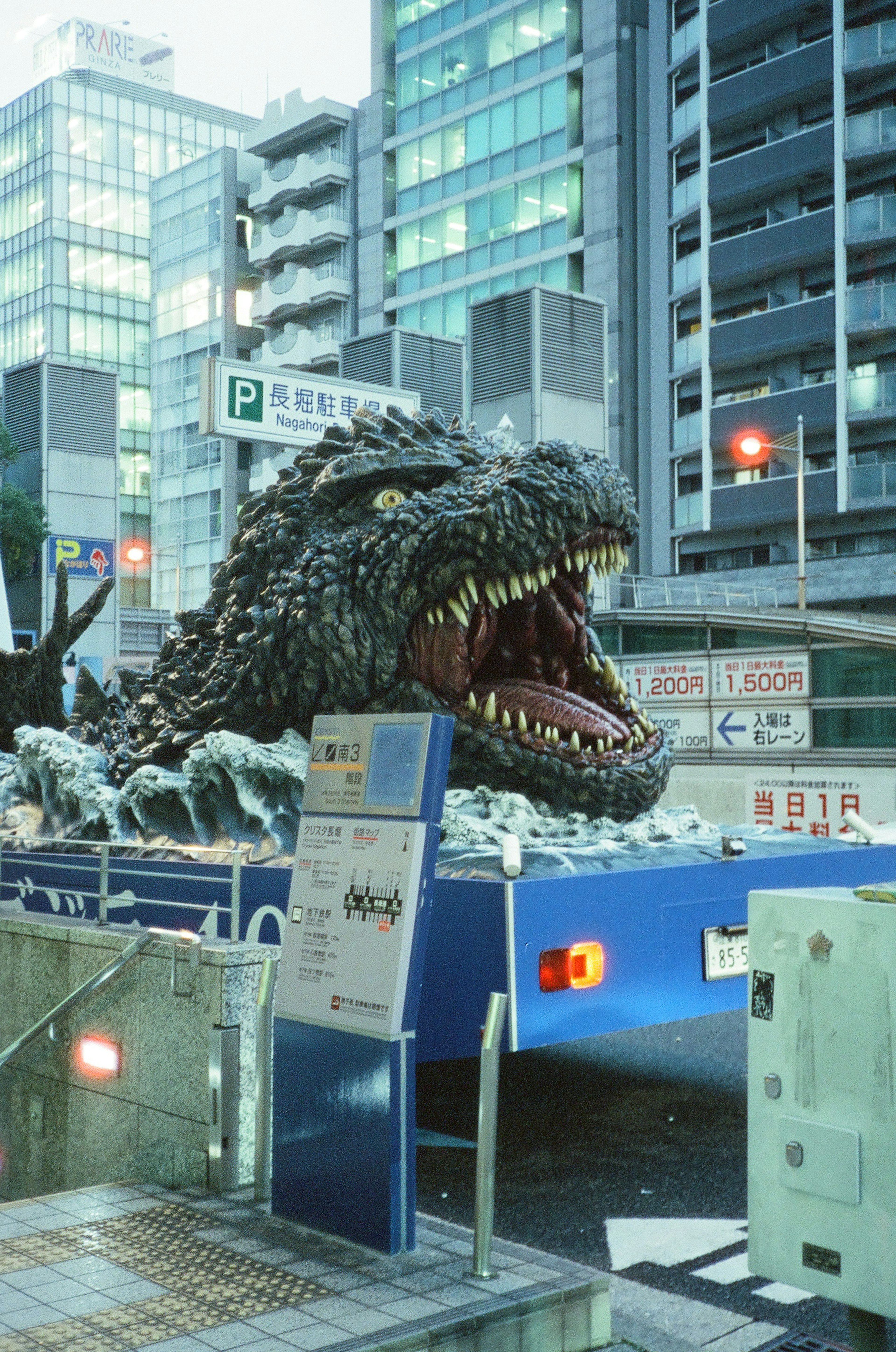 Una cabeza gigante de Godzilla emergiendo en el paisaje urbano de Tokio