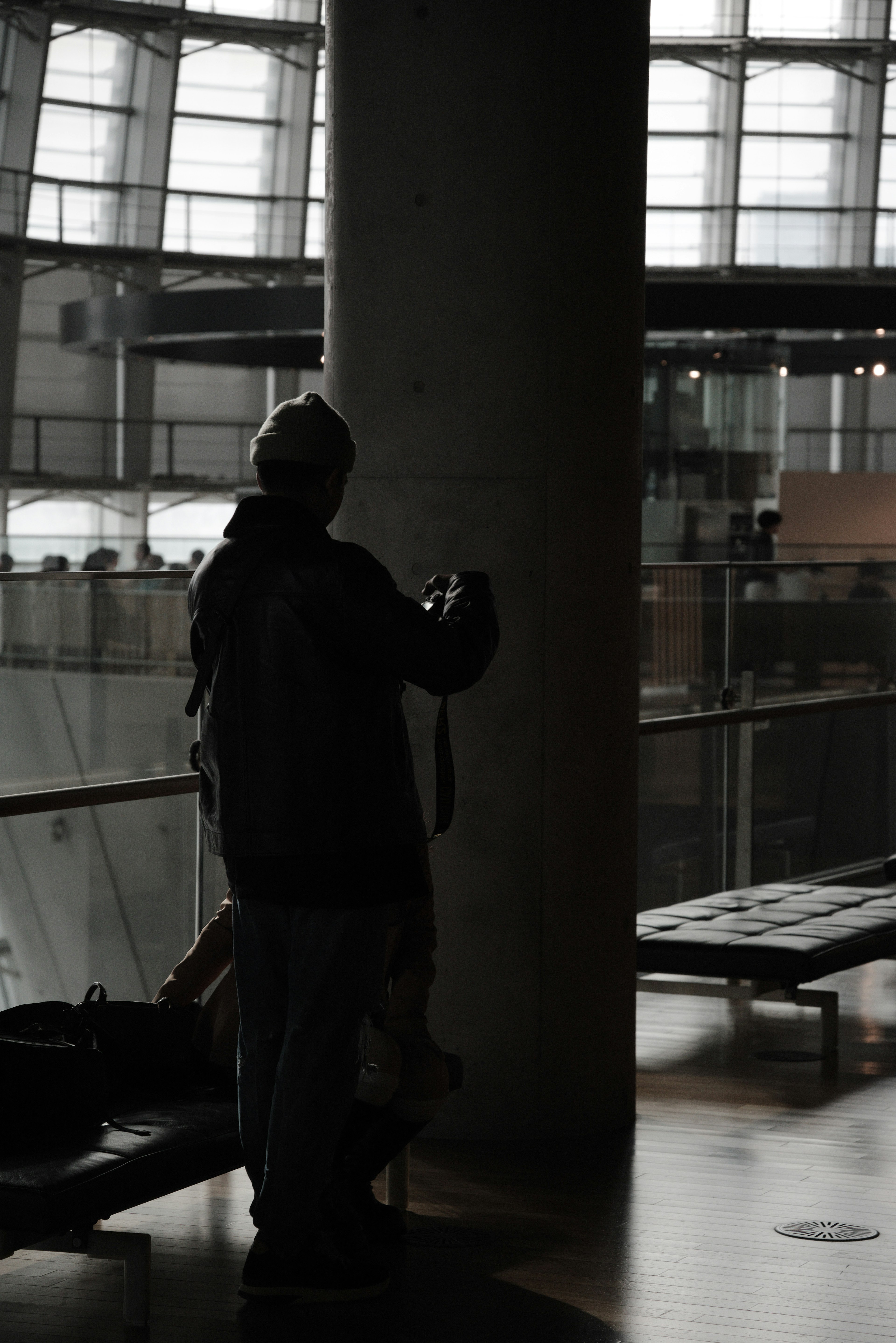 Silhouette of a person leaning against a pillar with modern architecture in the background