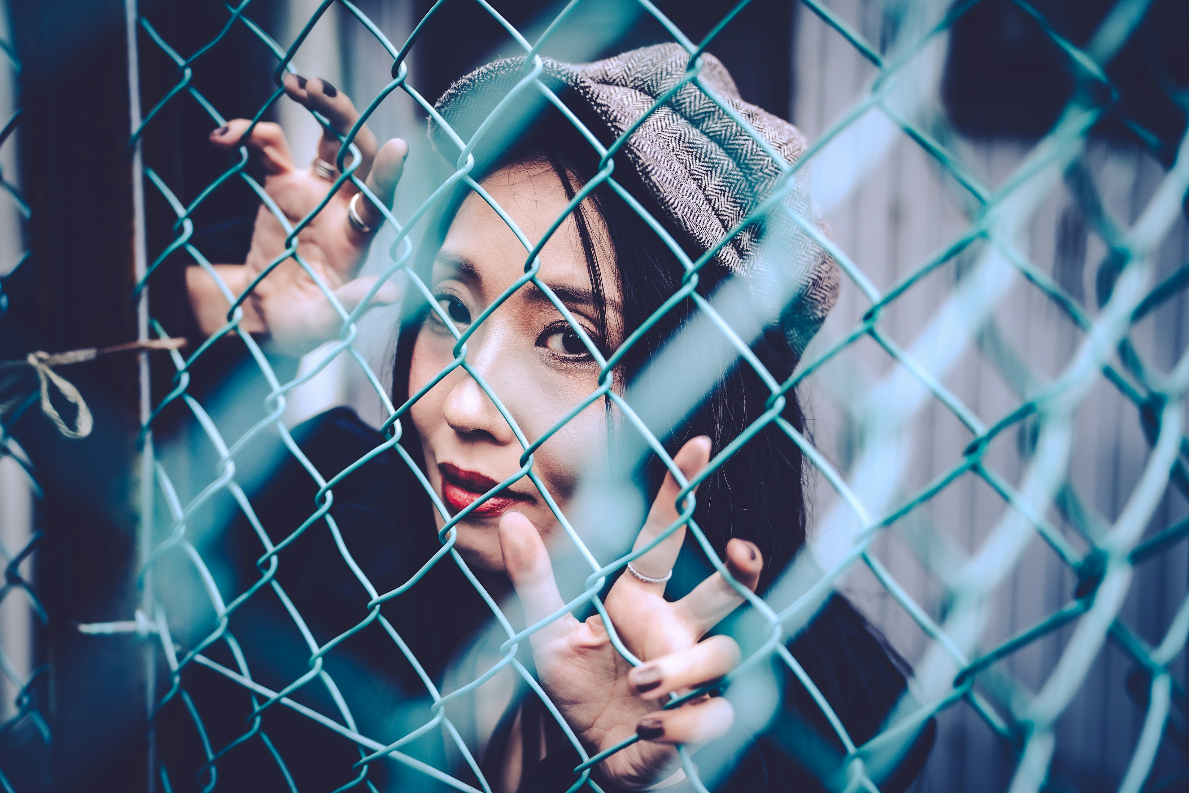 A woman gazing through a chain-link fence with a thoughtful expression