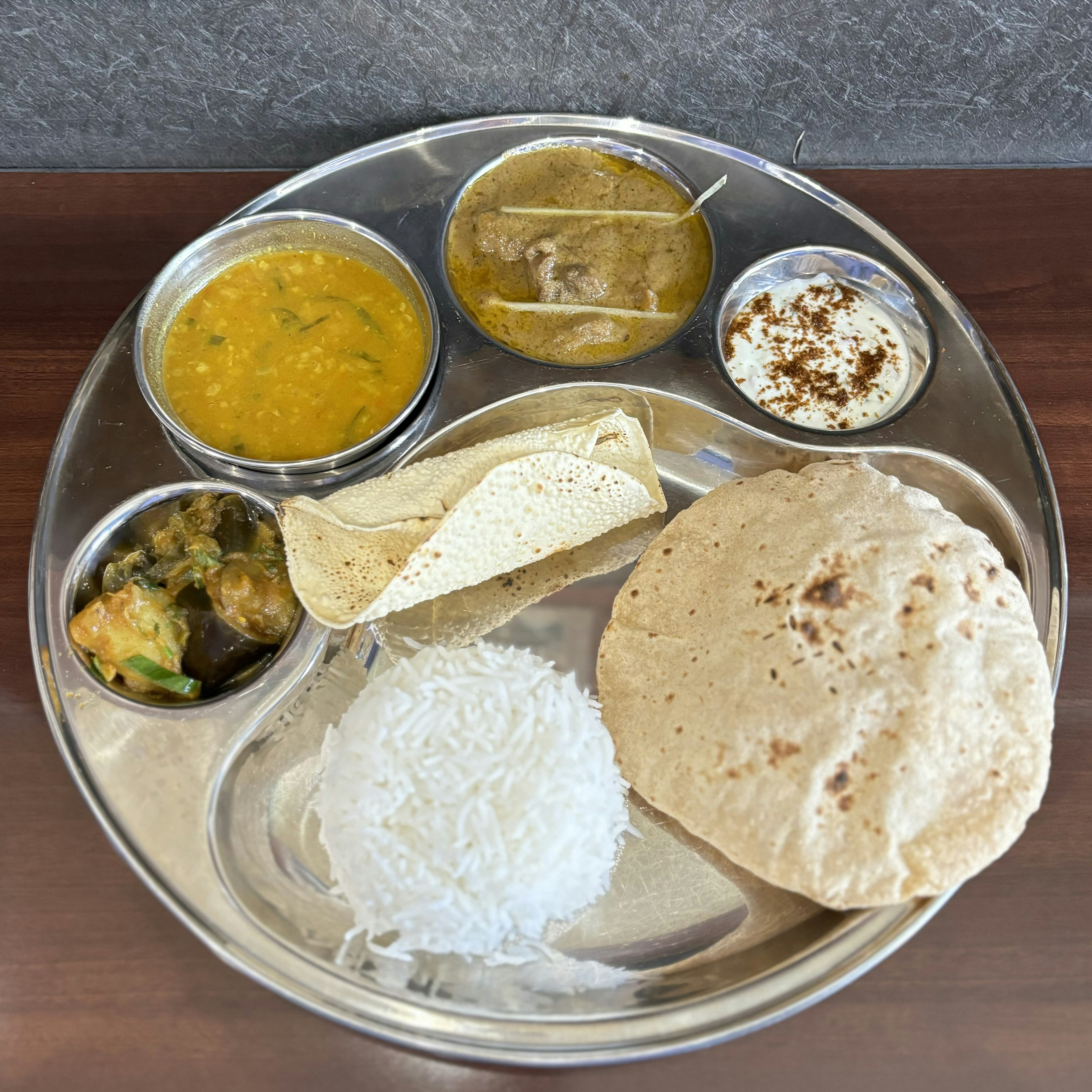 An Indian meal served on a plate including rice, roti, dal, curry, salad, and yogurt