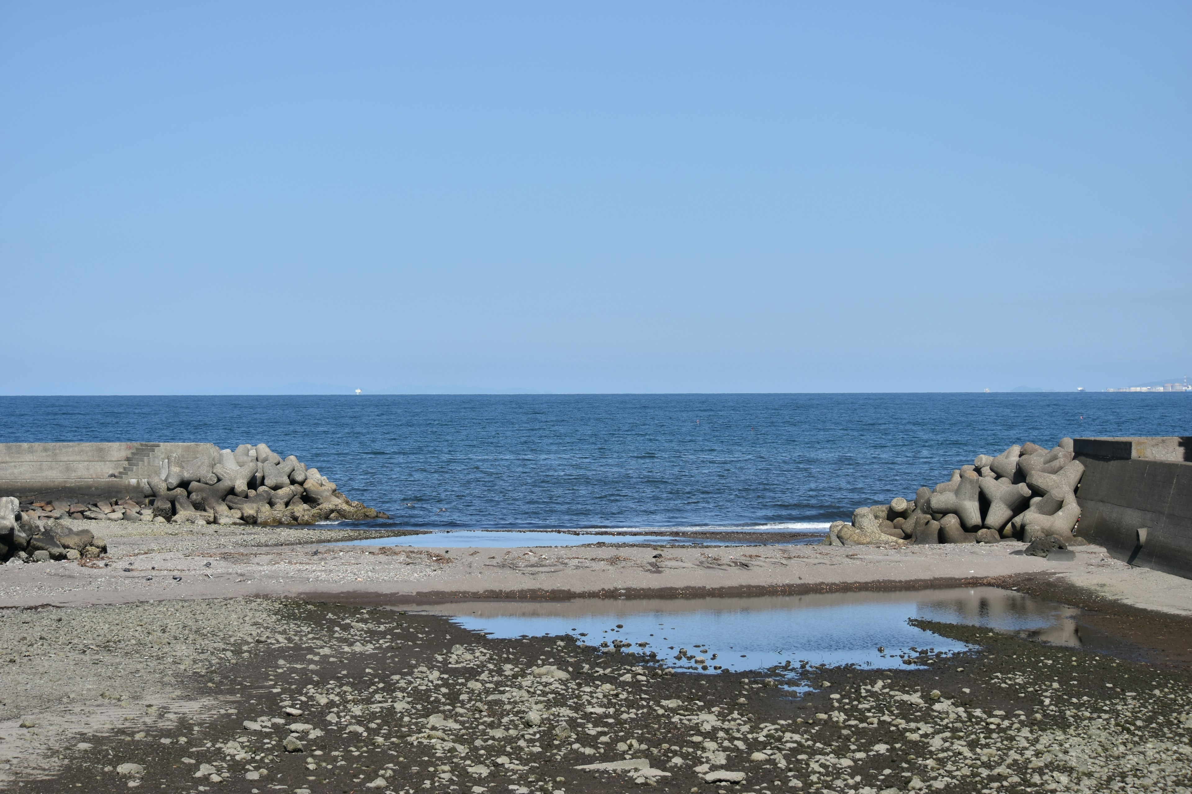 Eine ruhige Aussicht auf den blauen Ozean und den klaren Himmel mit einem Strand aus Steinen und einer Pfütze