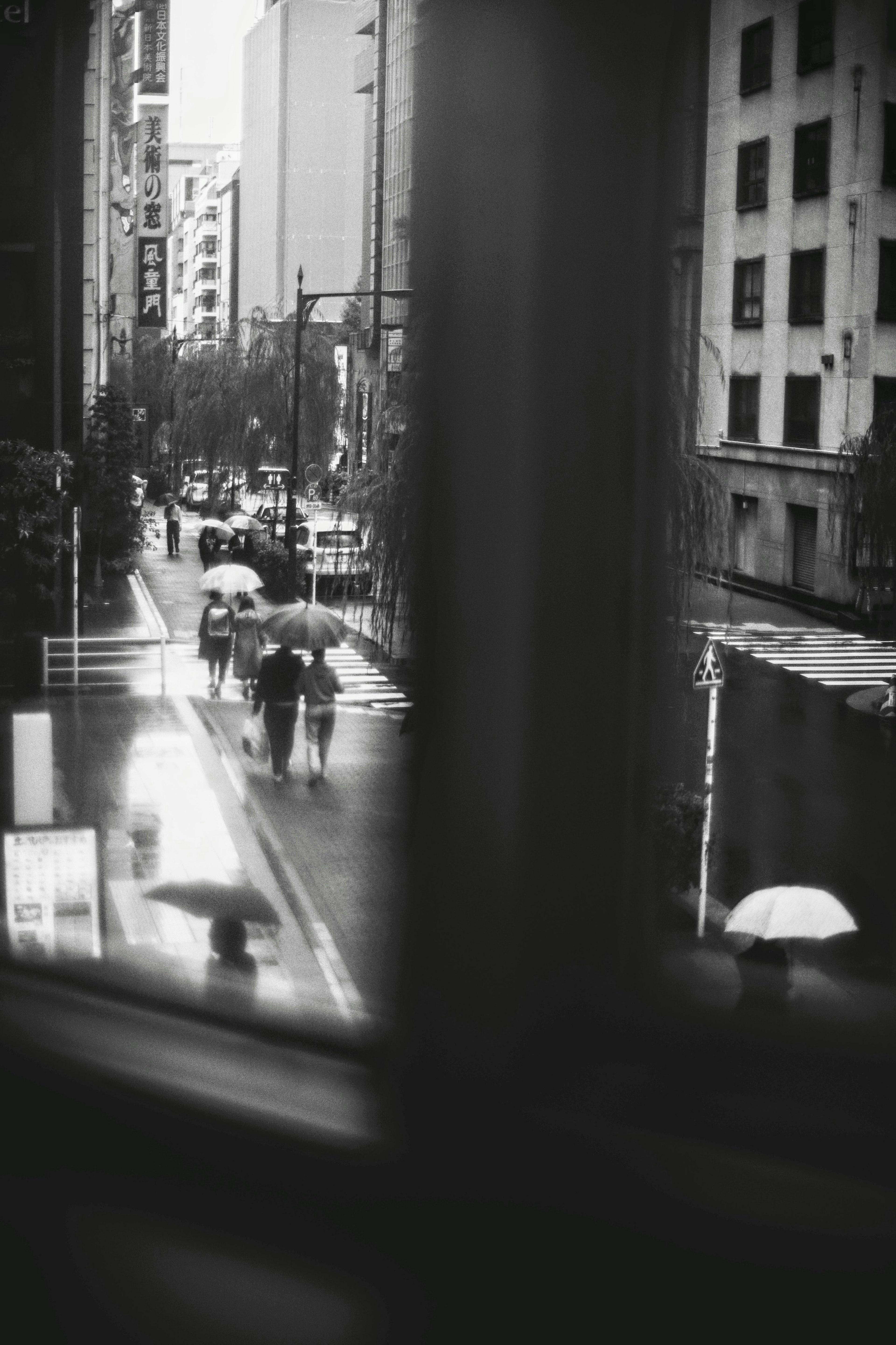 雨の中を歩く人々とビルが並ぶ街並みのモノクロ写真