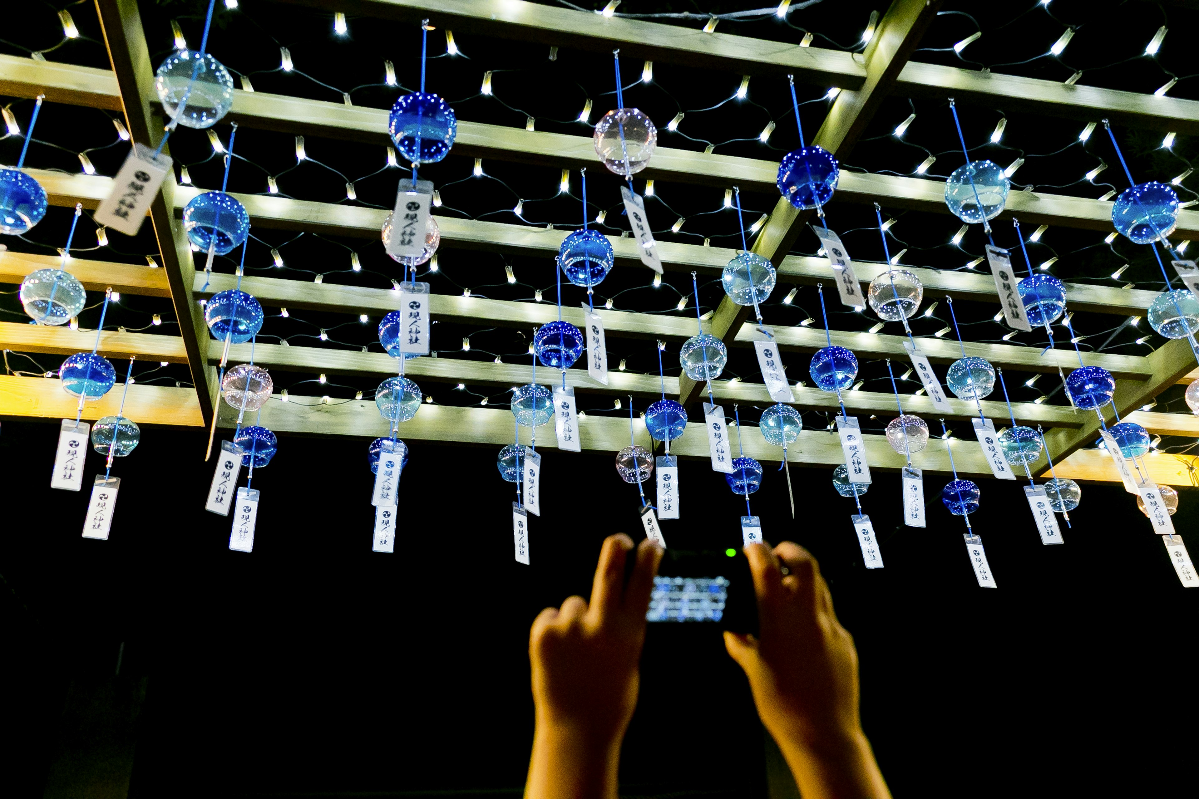 Hands holding a phone to capture blue wind chimes hanging in an outdoor space