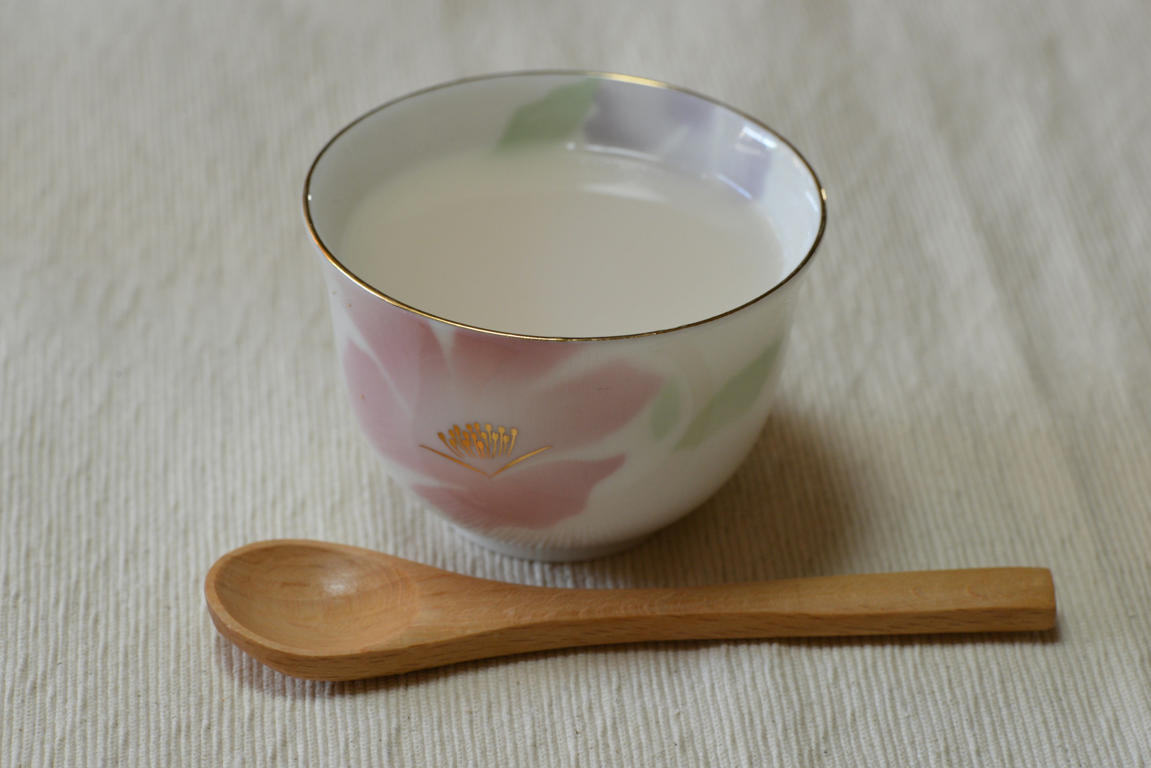 A beautiful flower-patterned bowl with a white drink and a wooden spoon