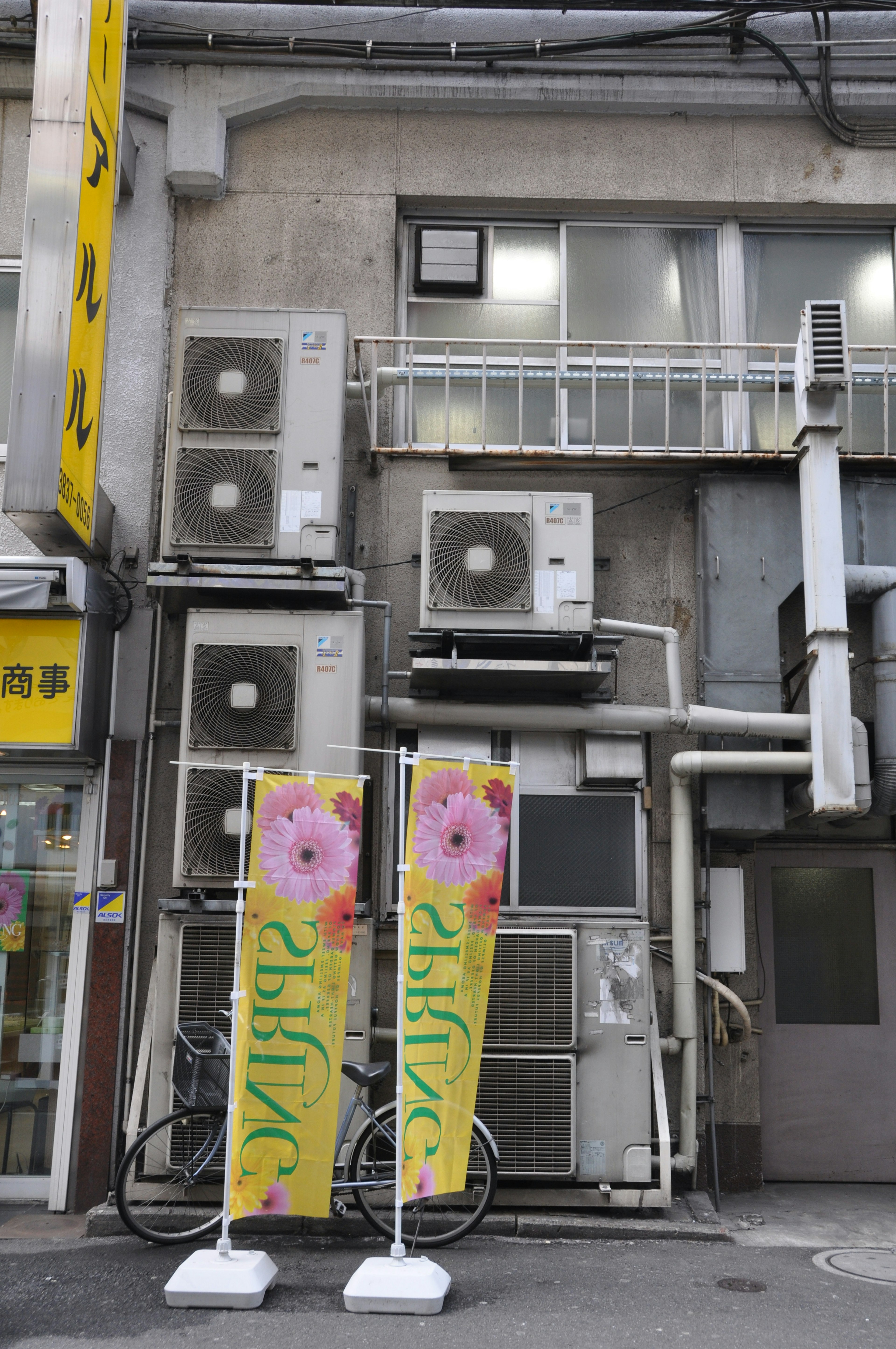 Fachada de un edificio con múltiples unidades de aire acondicionado y pancartas florales