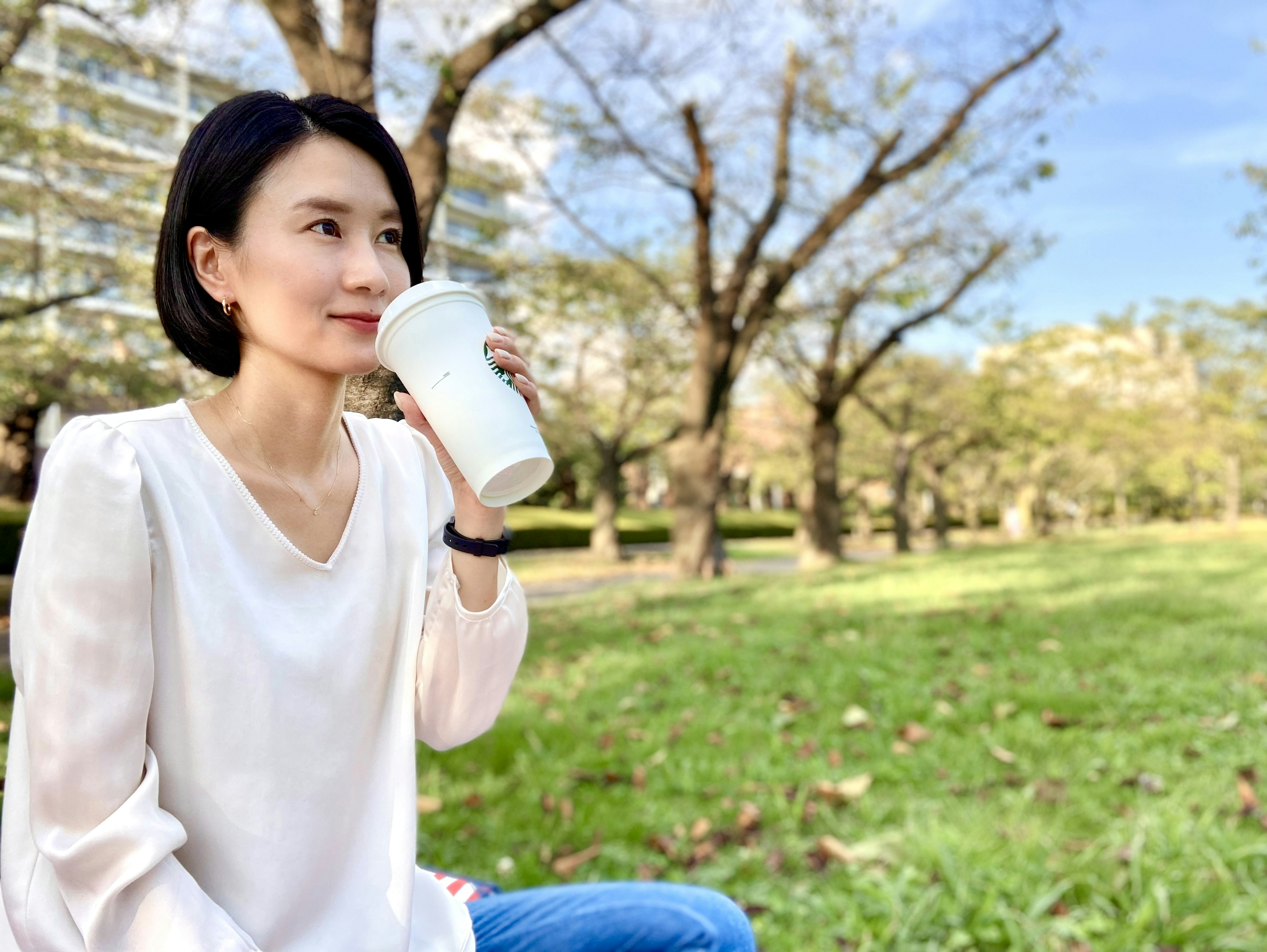 Woman enjoying coffee in a park with trees in the background