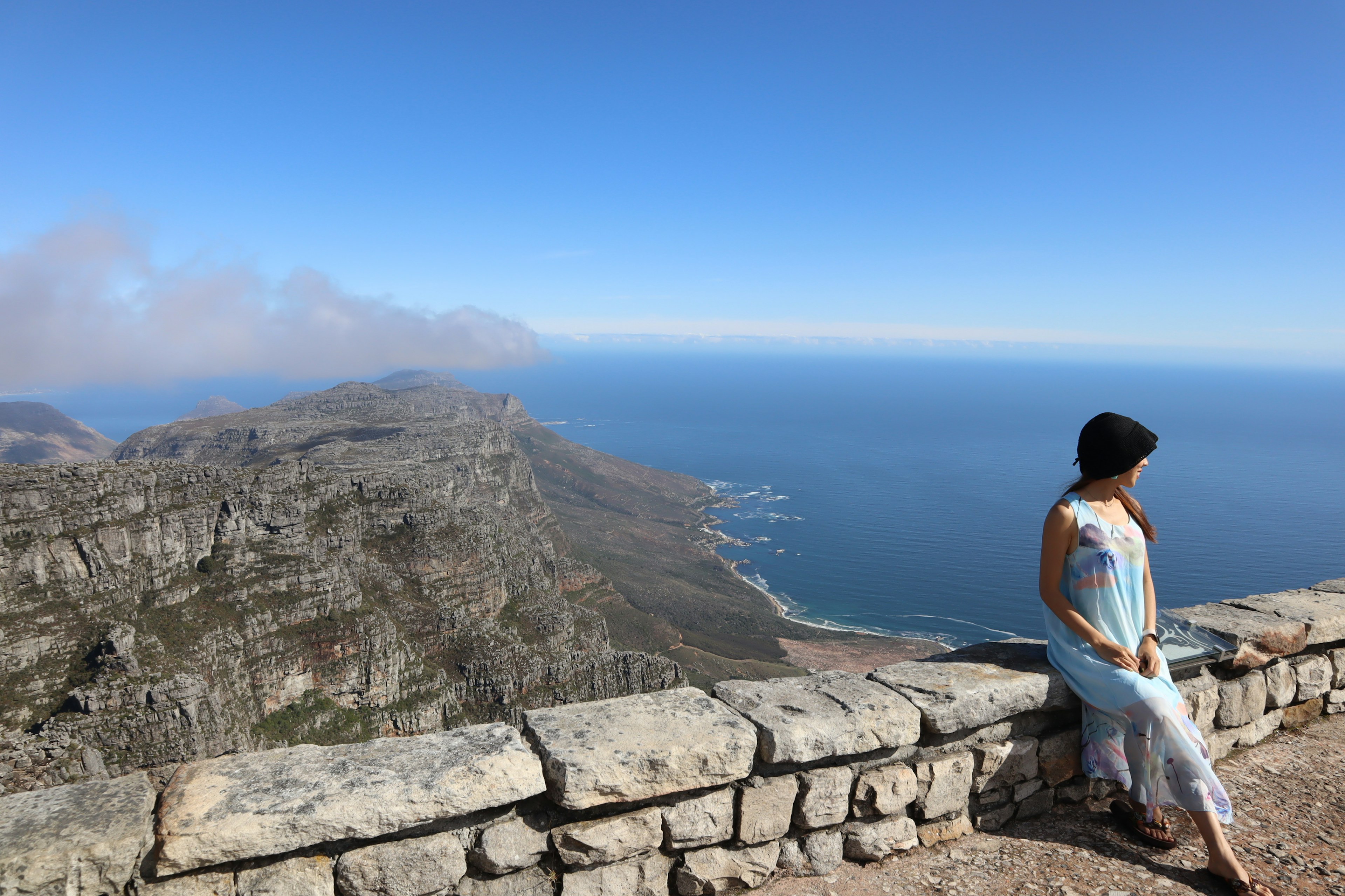 A woman leaning against a stone wall with a stunning view of the ocean and mountains