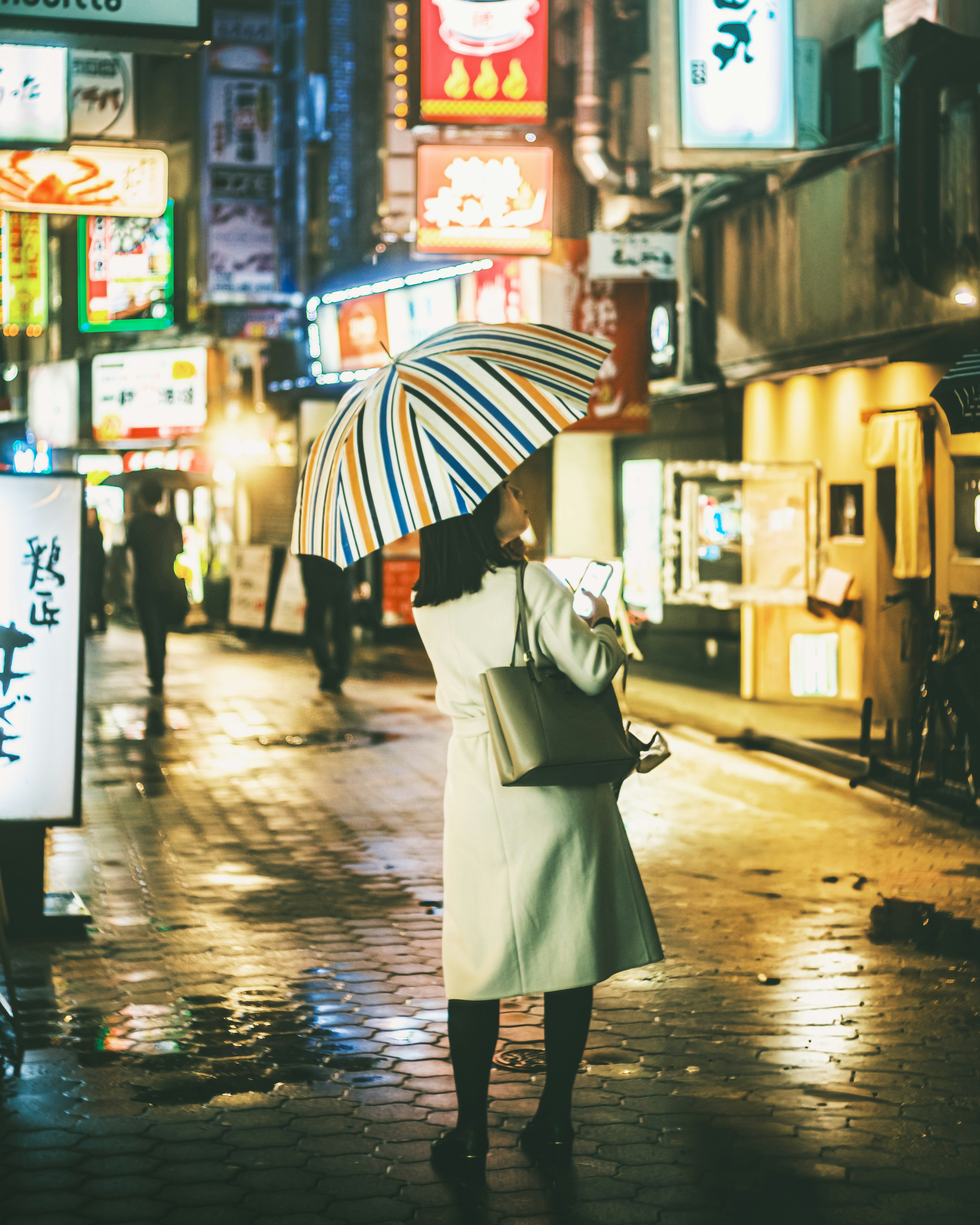 一位女性在雨夜的街道上走，手持雨伞