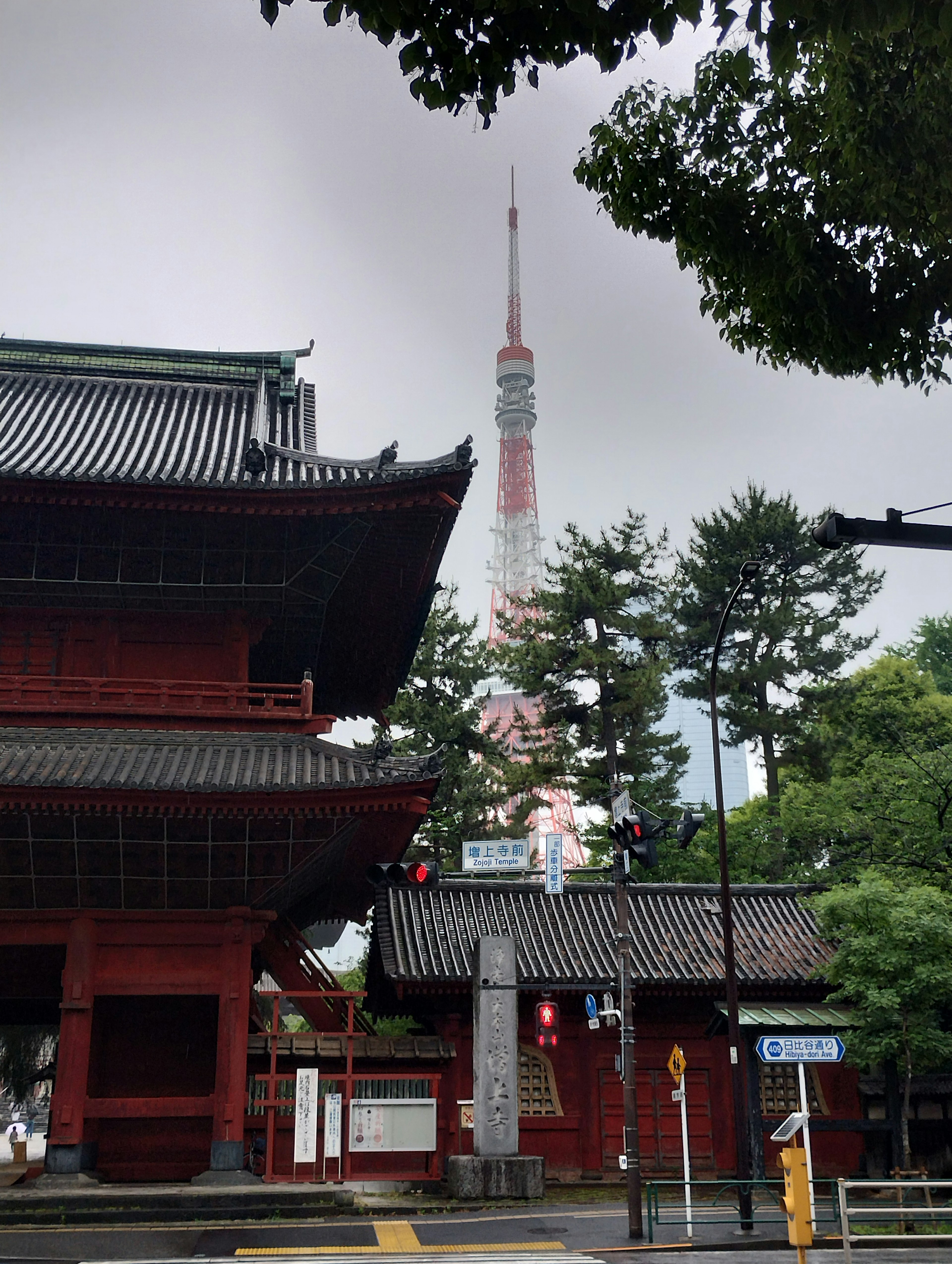 Bangunan tradisional merah dengan Menara Tokyo di latar belakang dan pohon hijau