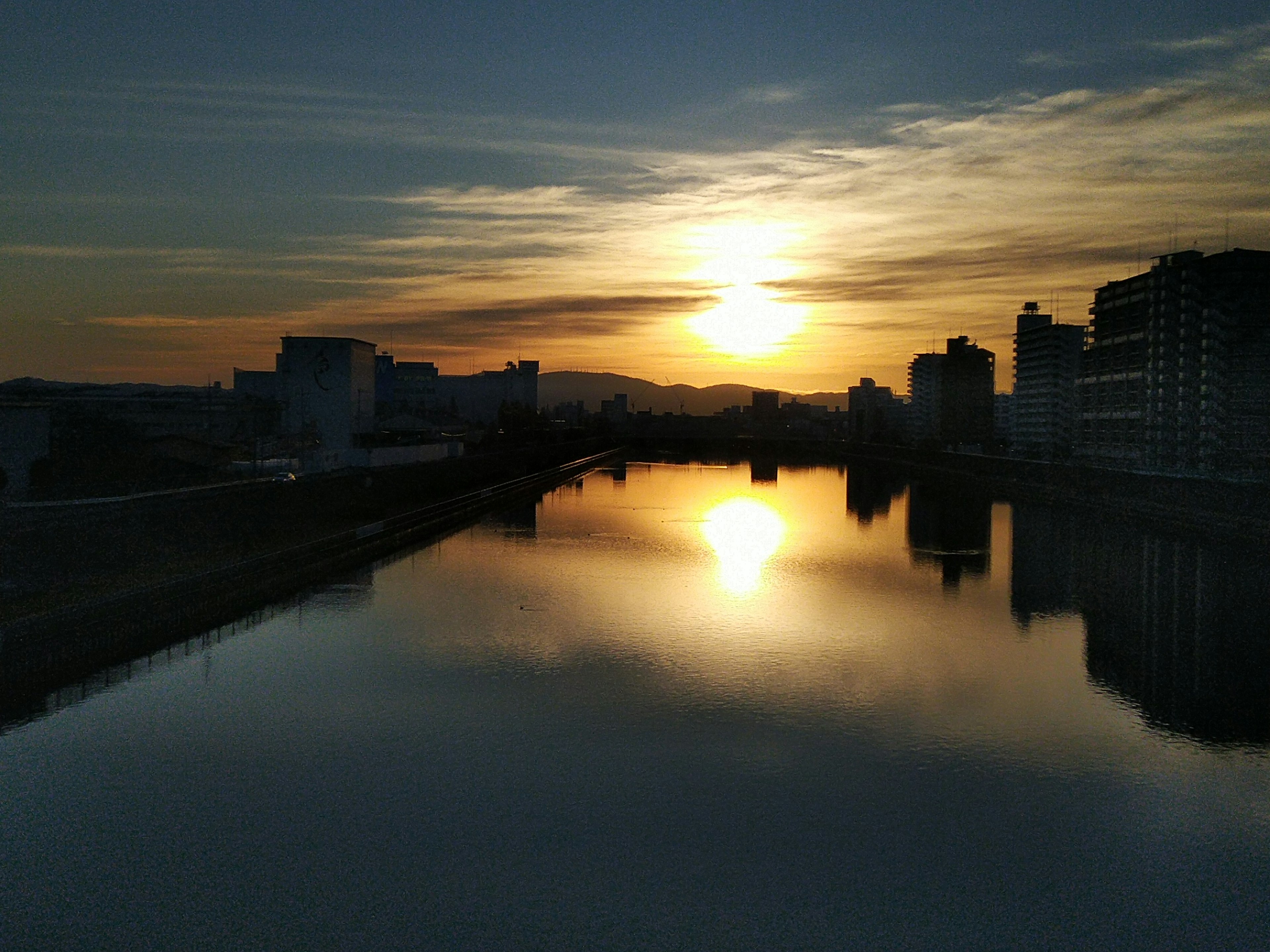 Schöner Sonnenuntergang, der sich im Fluss spiegelt, Skyline mit Gebäuden und ruhigem Wasser