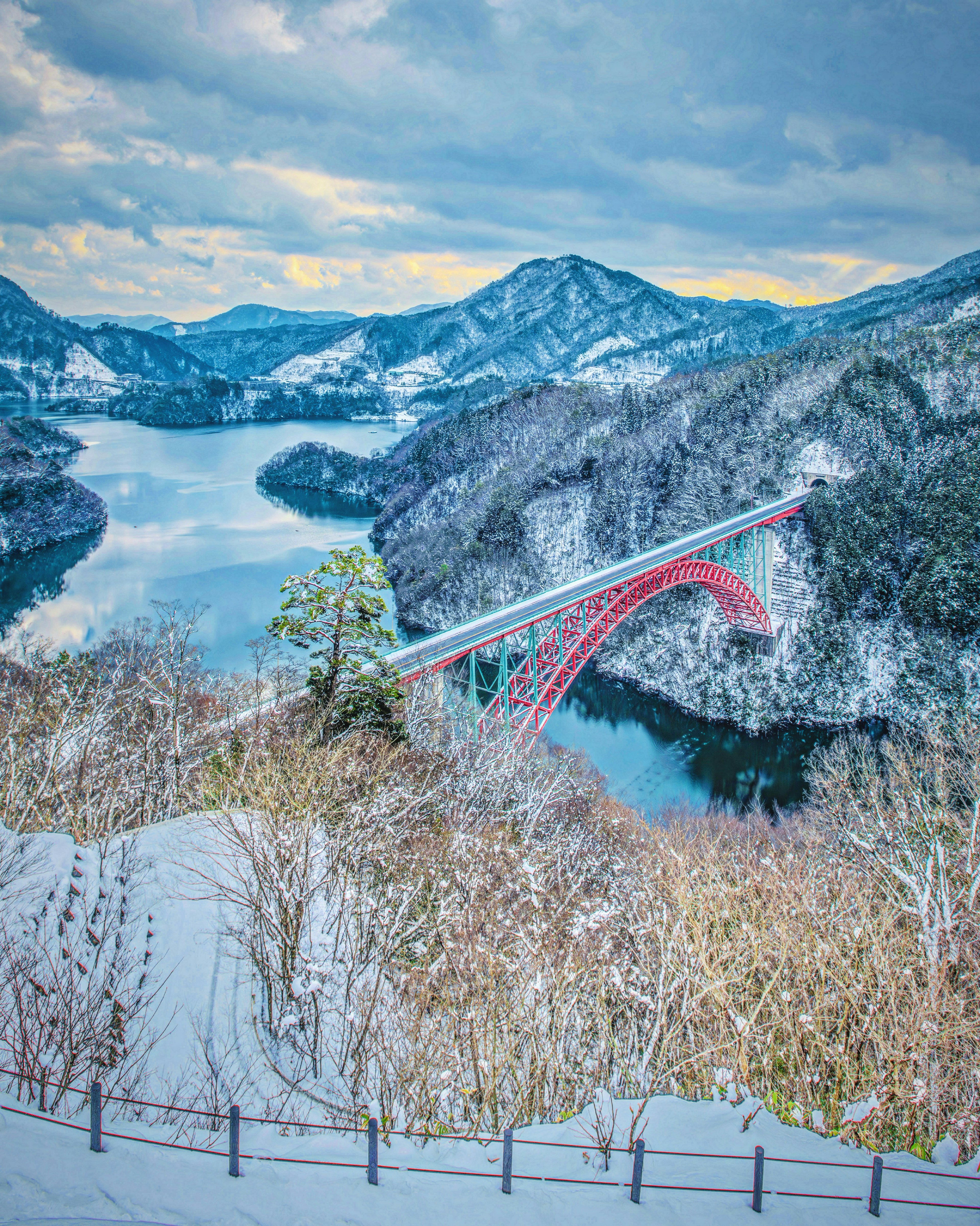 Vista panoramica di un ponte rosso su un paesaggio innevato con montagne e lago