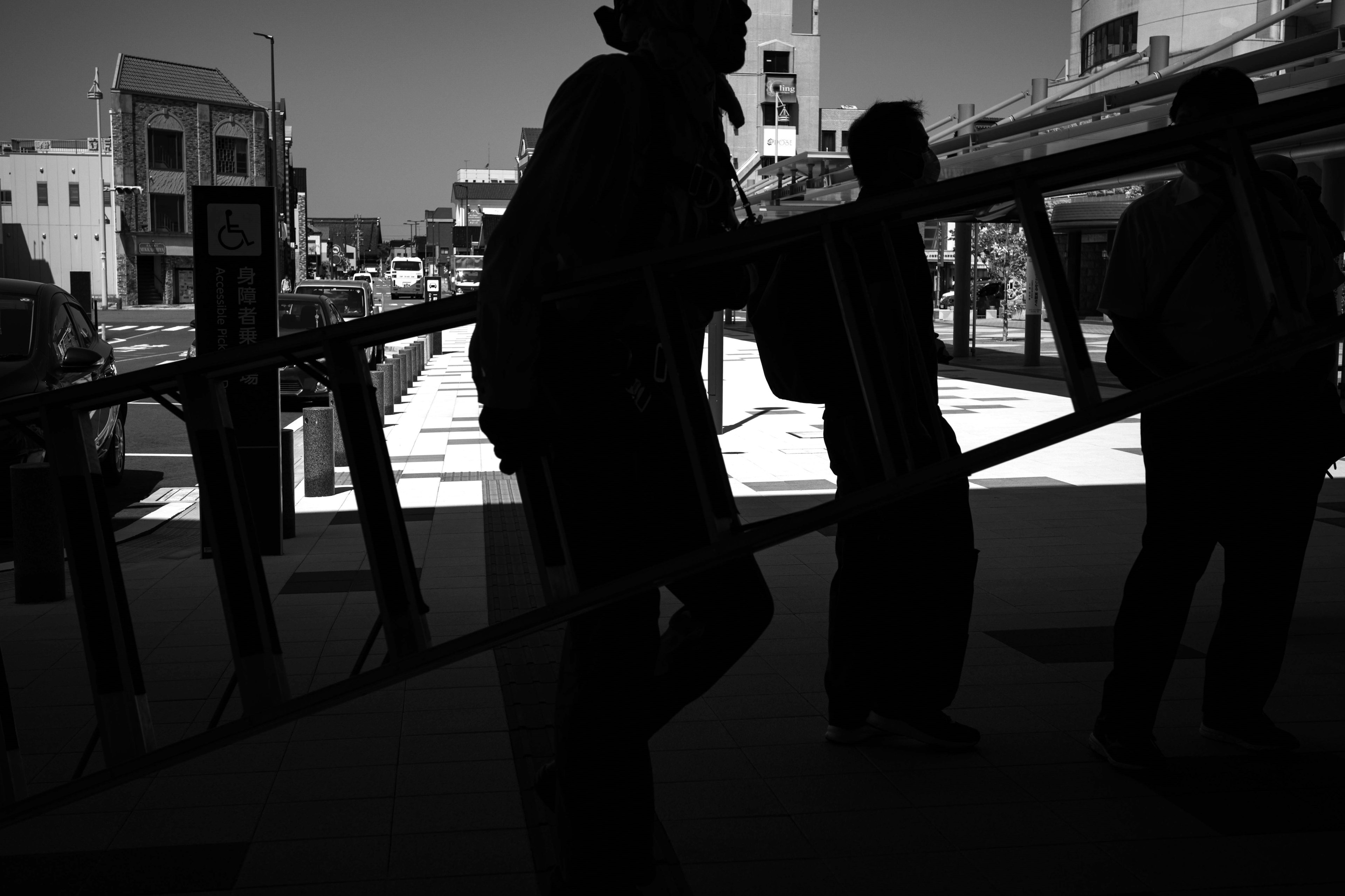 Silhouettes of people carrying a ladder in an urban setting