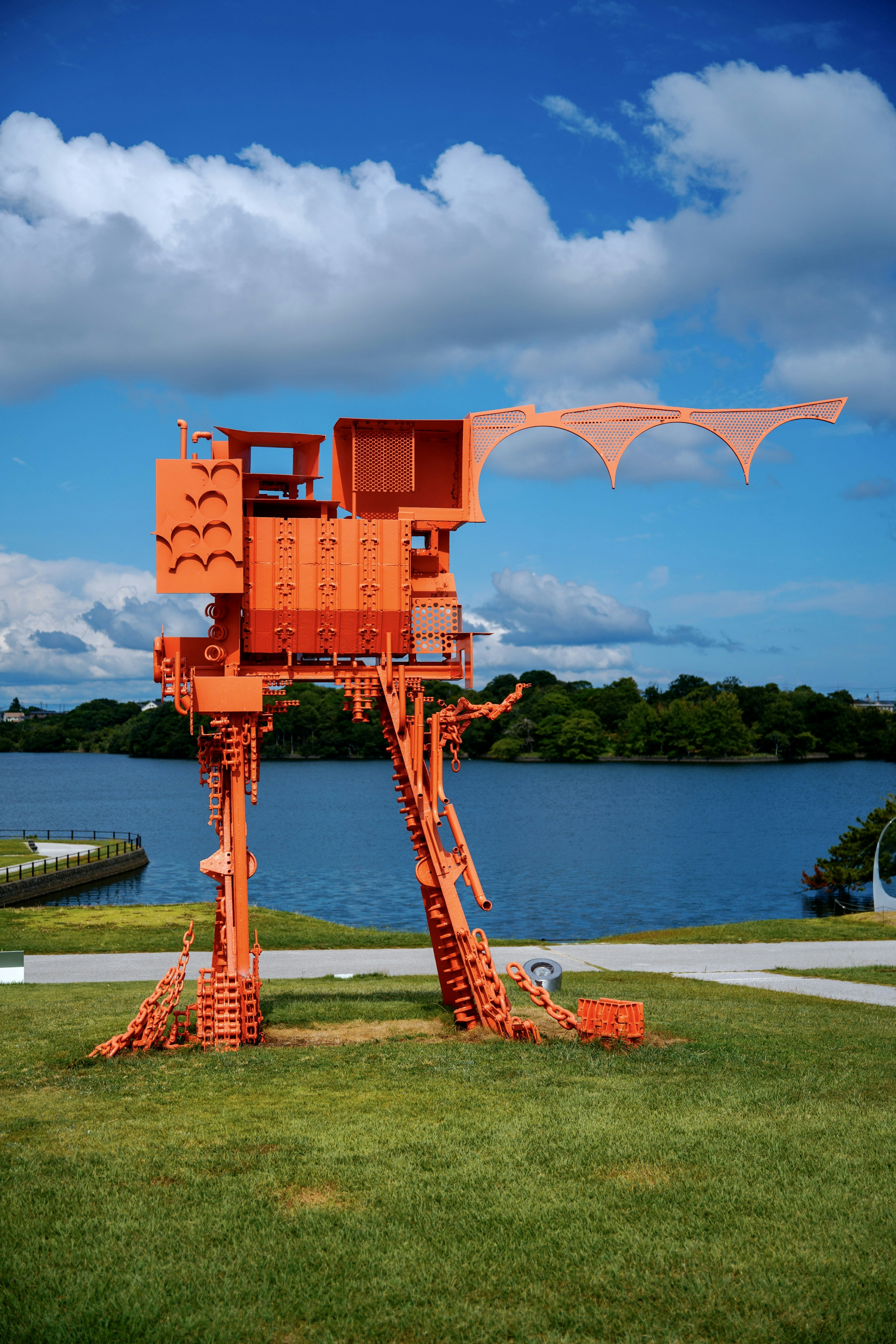 Orange art installation with a lake and blue sky in the background