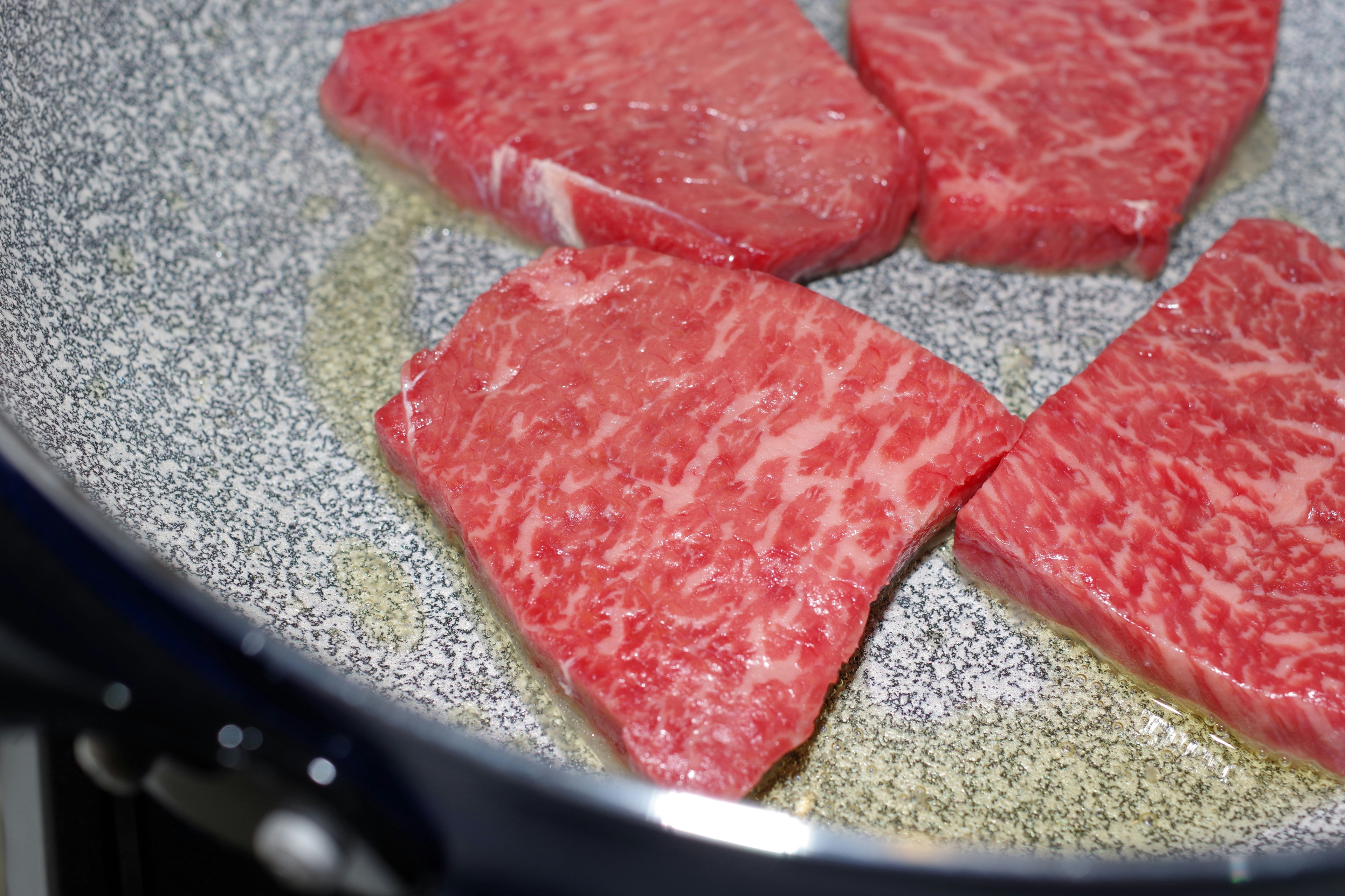 Piezas de carne veteada cocinándose en una sartén