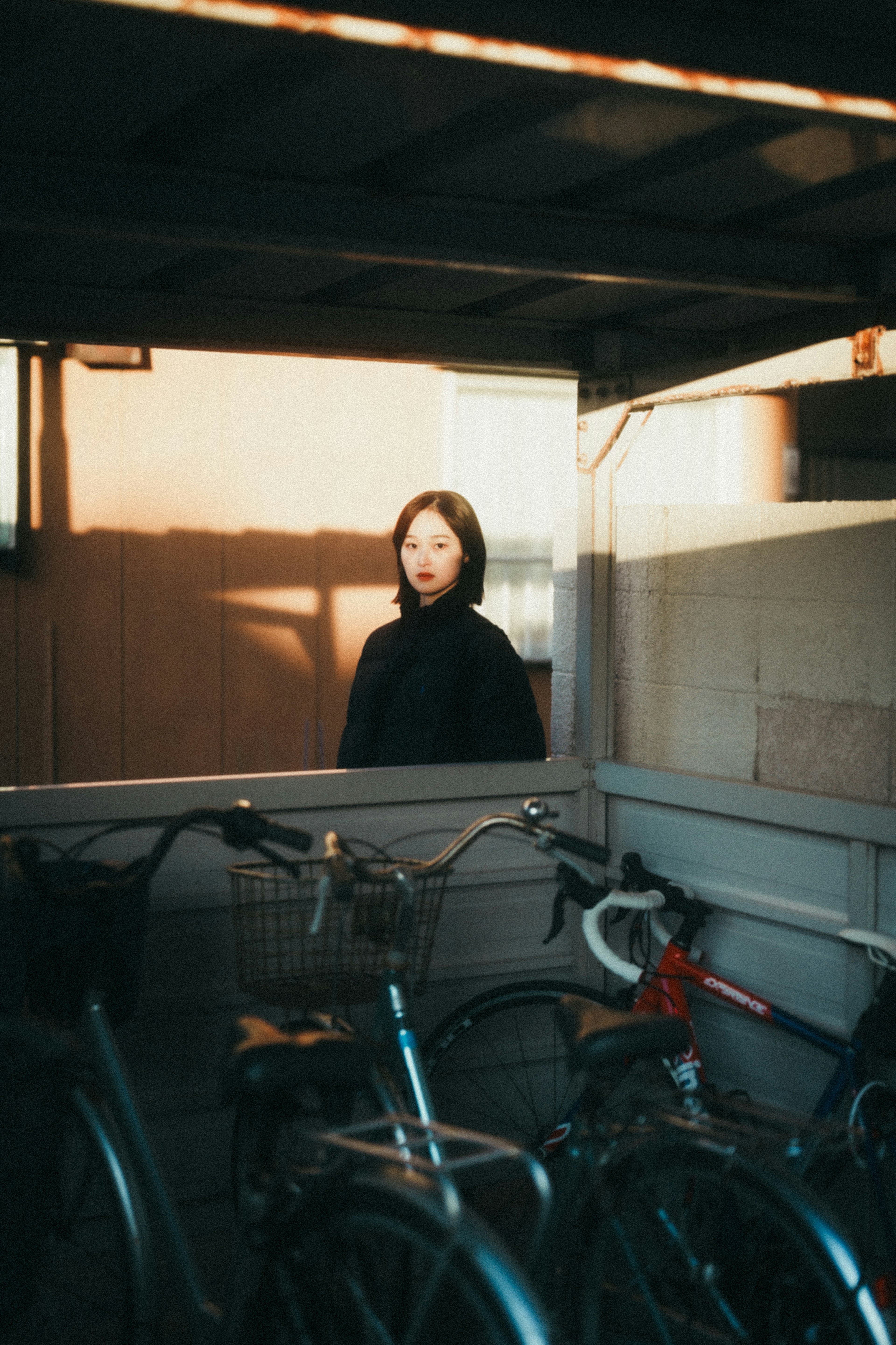 Una mujer de pie frente a bicicletas con un fondo oscuro y un impresionante contraste de luz