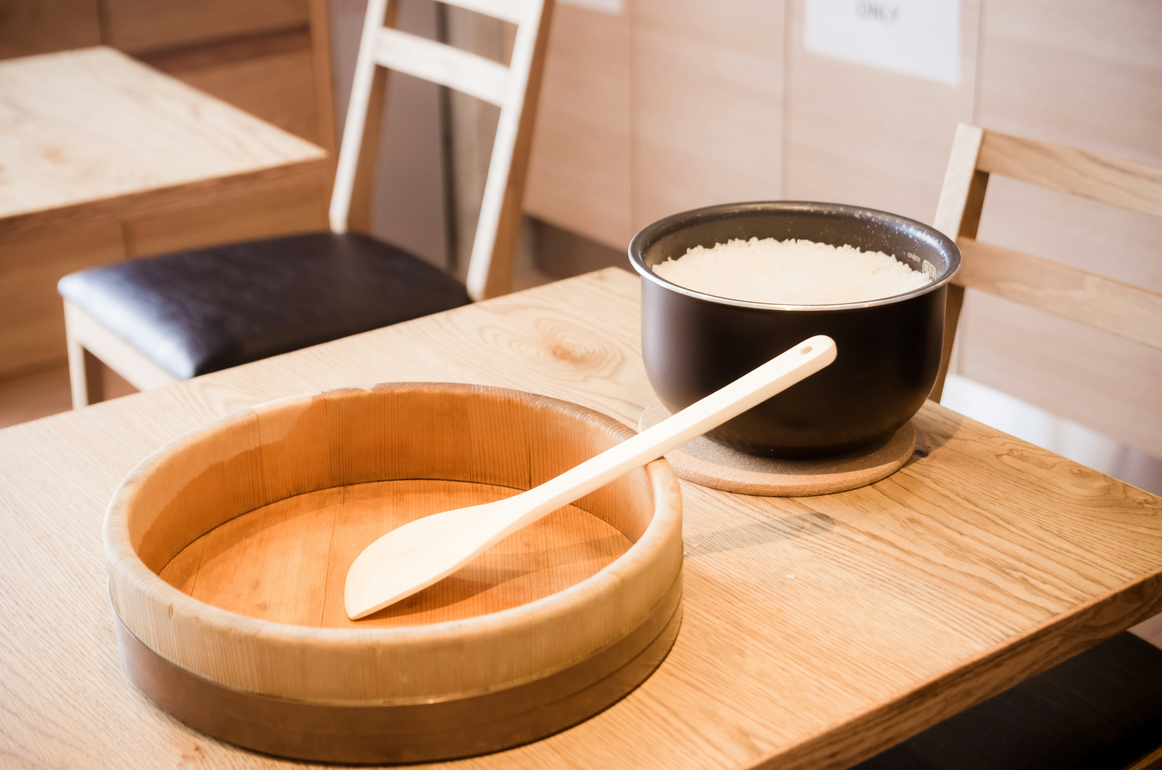 Holzschüssel und Löffel auf einem Tisch mit einem schwarzen Topf Reis