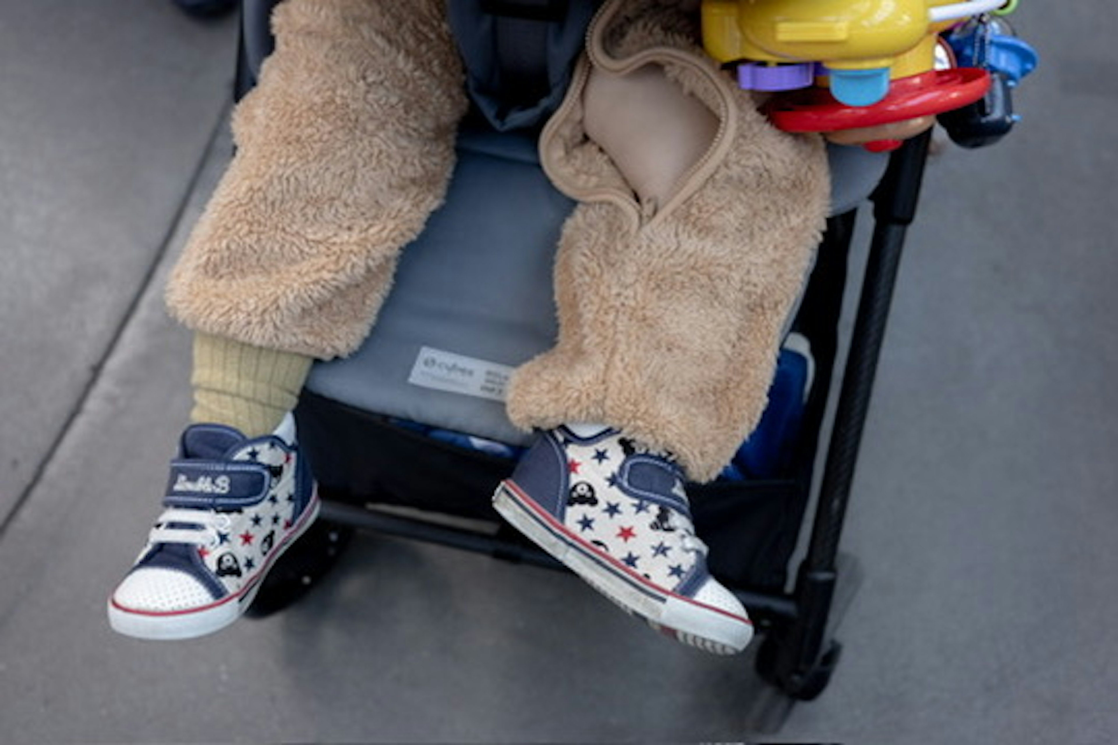 Close-up of a child's feet in a stroller wearing beige pants and colorful sneakers