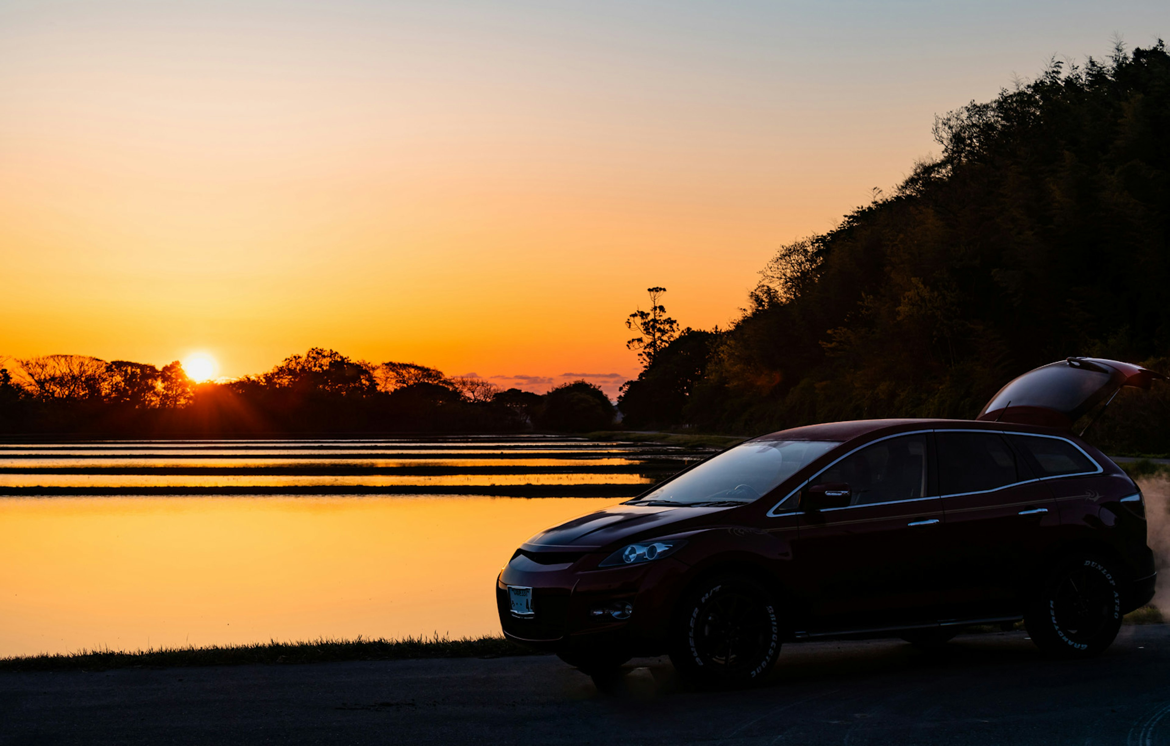 Black SUV parked by a lake during sunset