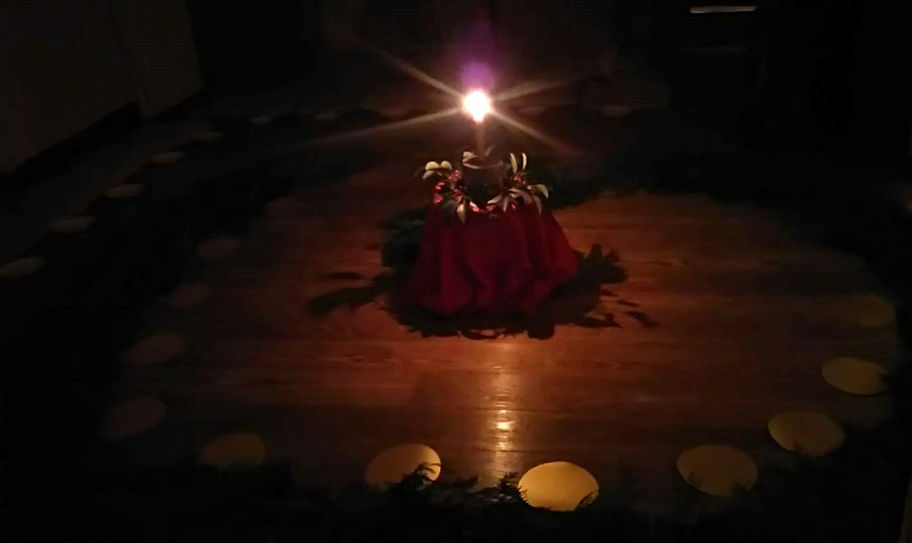 A dimly lit room featuring a central altar with a red tablecloth surrounded by circularly arranged stones