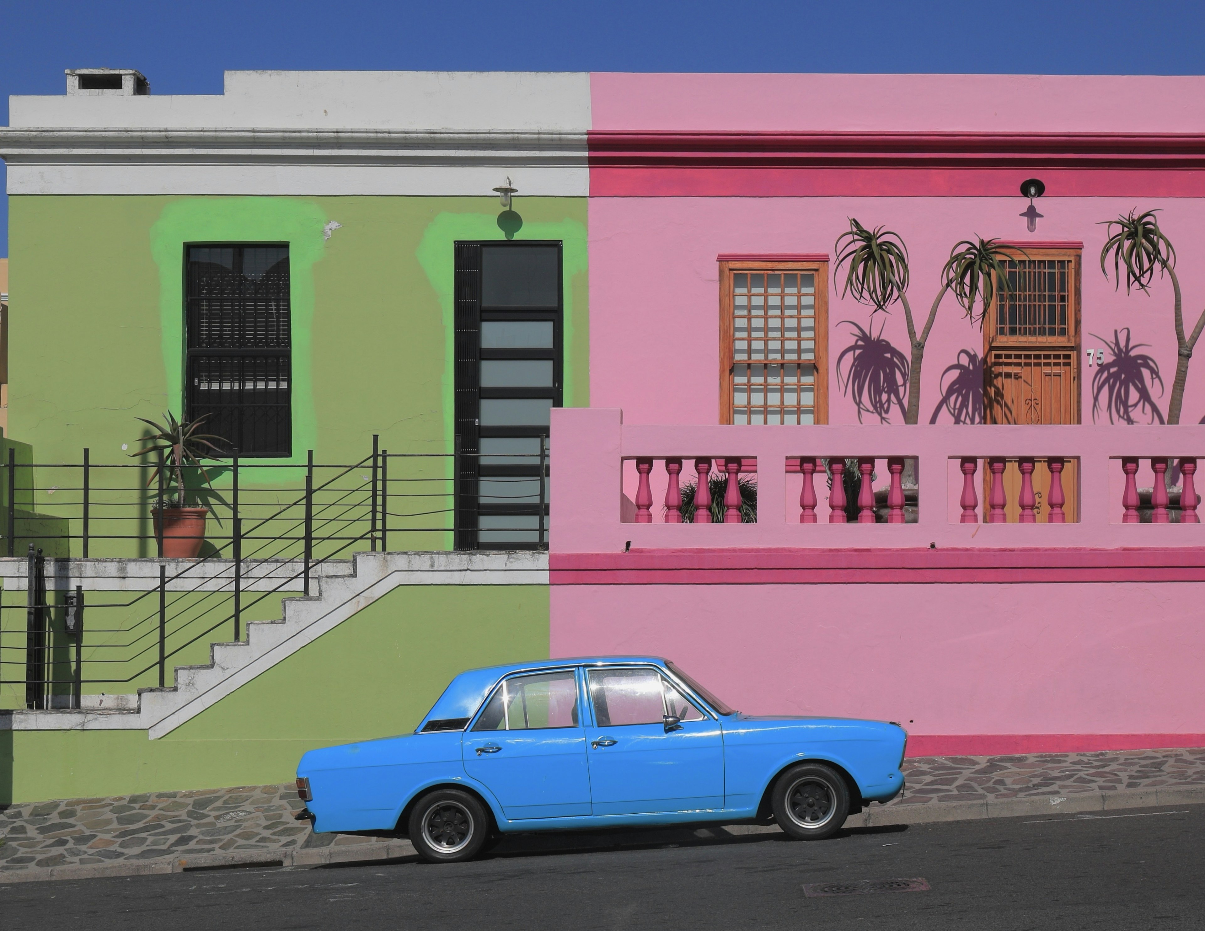 A blue car parked in front of colorful houses with green and pink walls