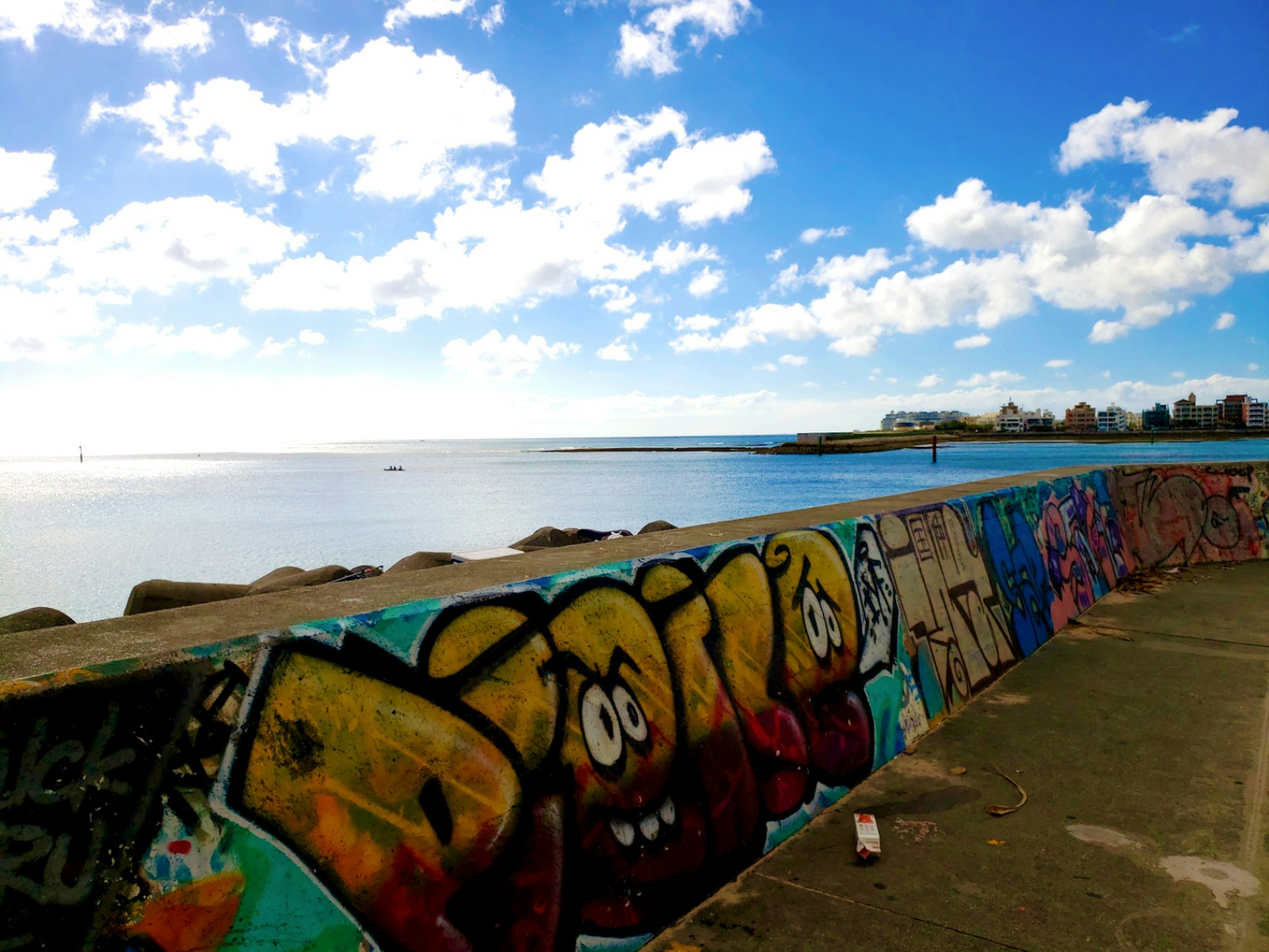 Bunter Graffiti-Wall mit lebhaften Buchstaben unter einem blauen Himmel und Wolken, die auf ein ruhiges Meer blicken