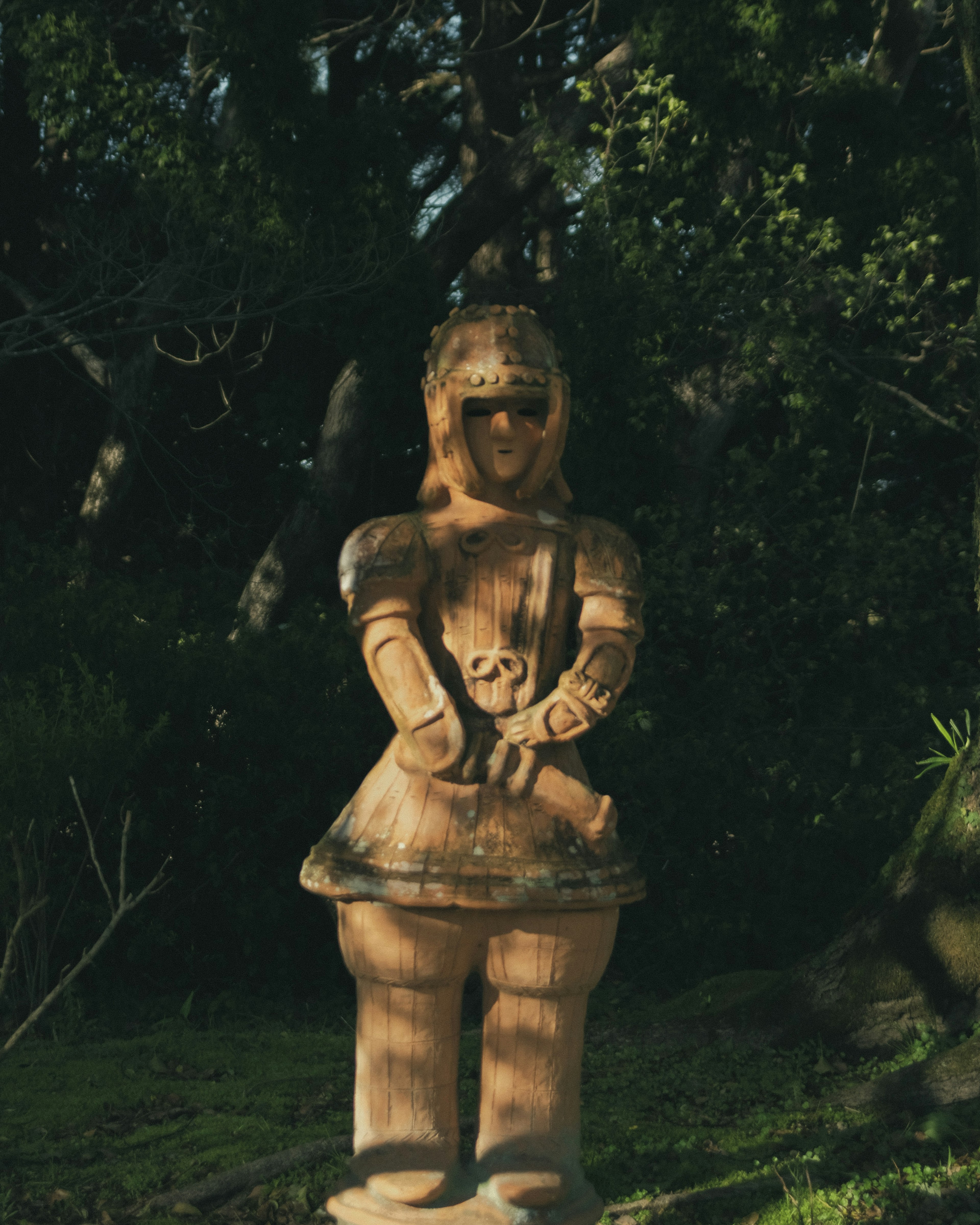 Wooden sculpture of a woman holding a skull surrounded by greenery