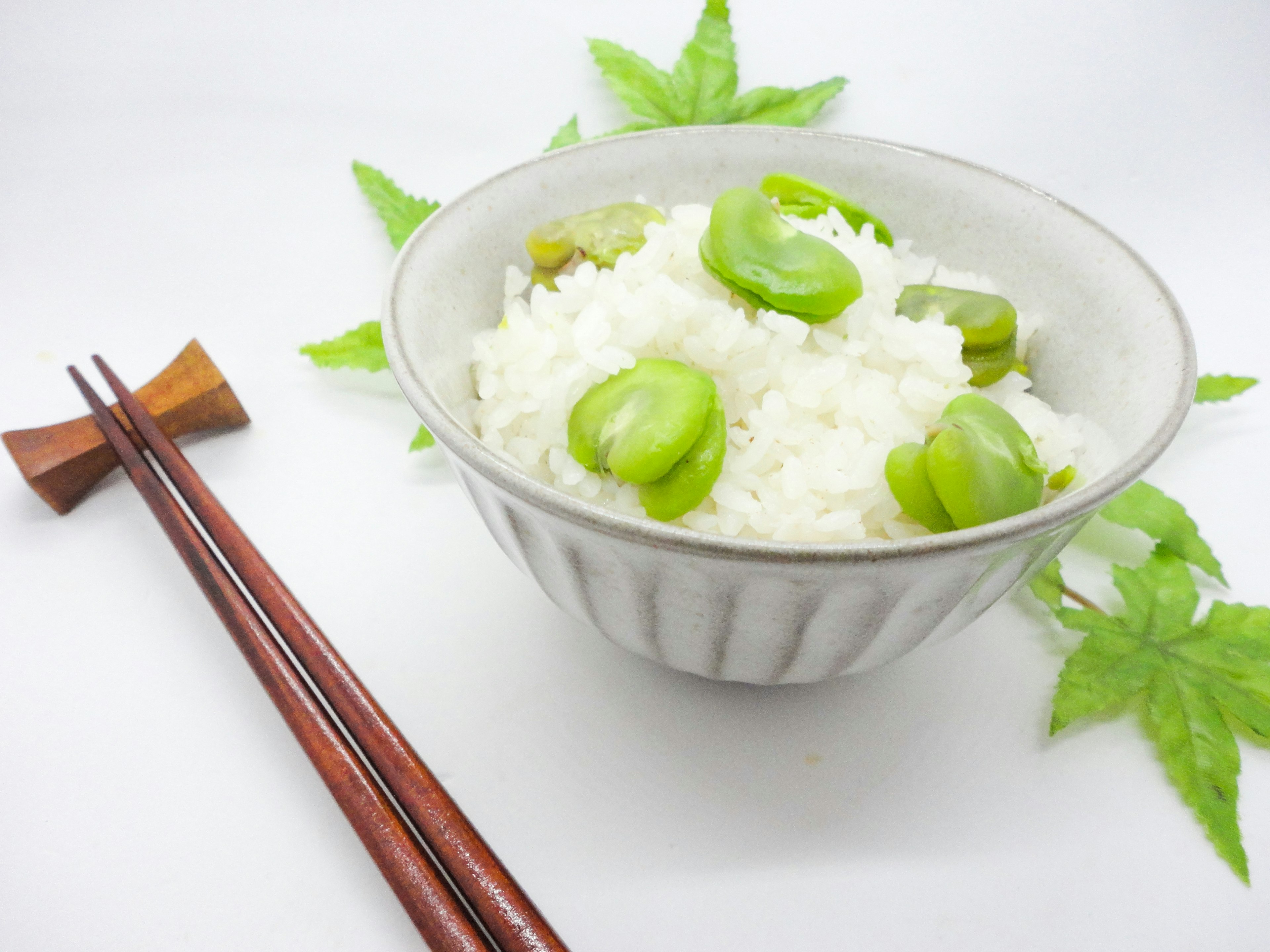 Mangkok nasi putih dengan kacang hijau dikelilingi daun dekoratif