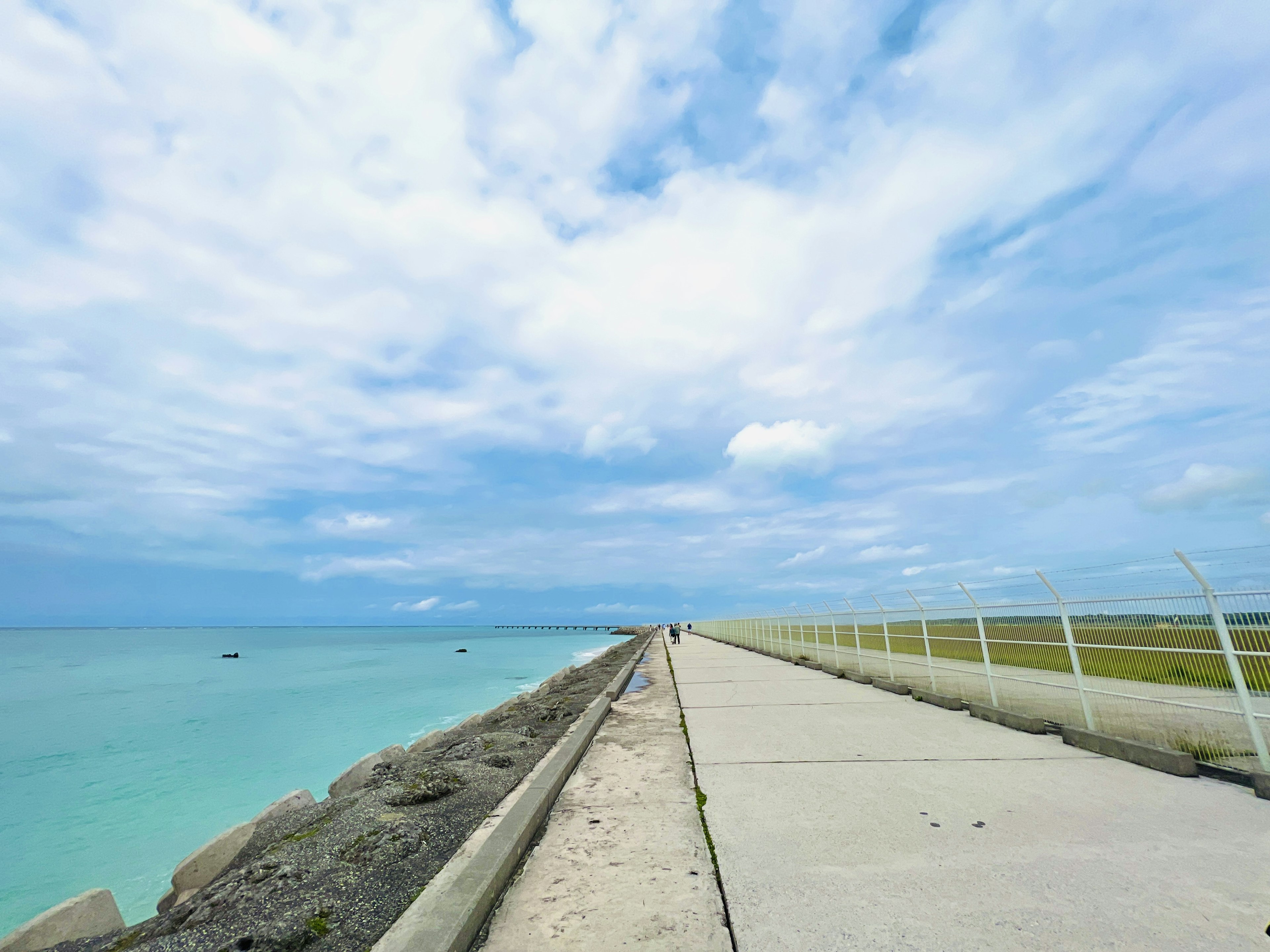 Camino de concreto que lleva a un mar azul bajo un cielo nublado