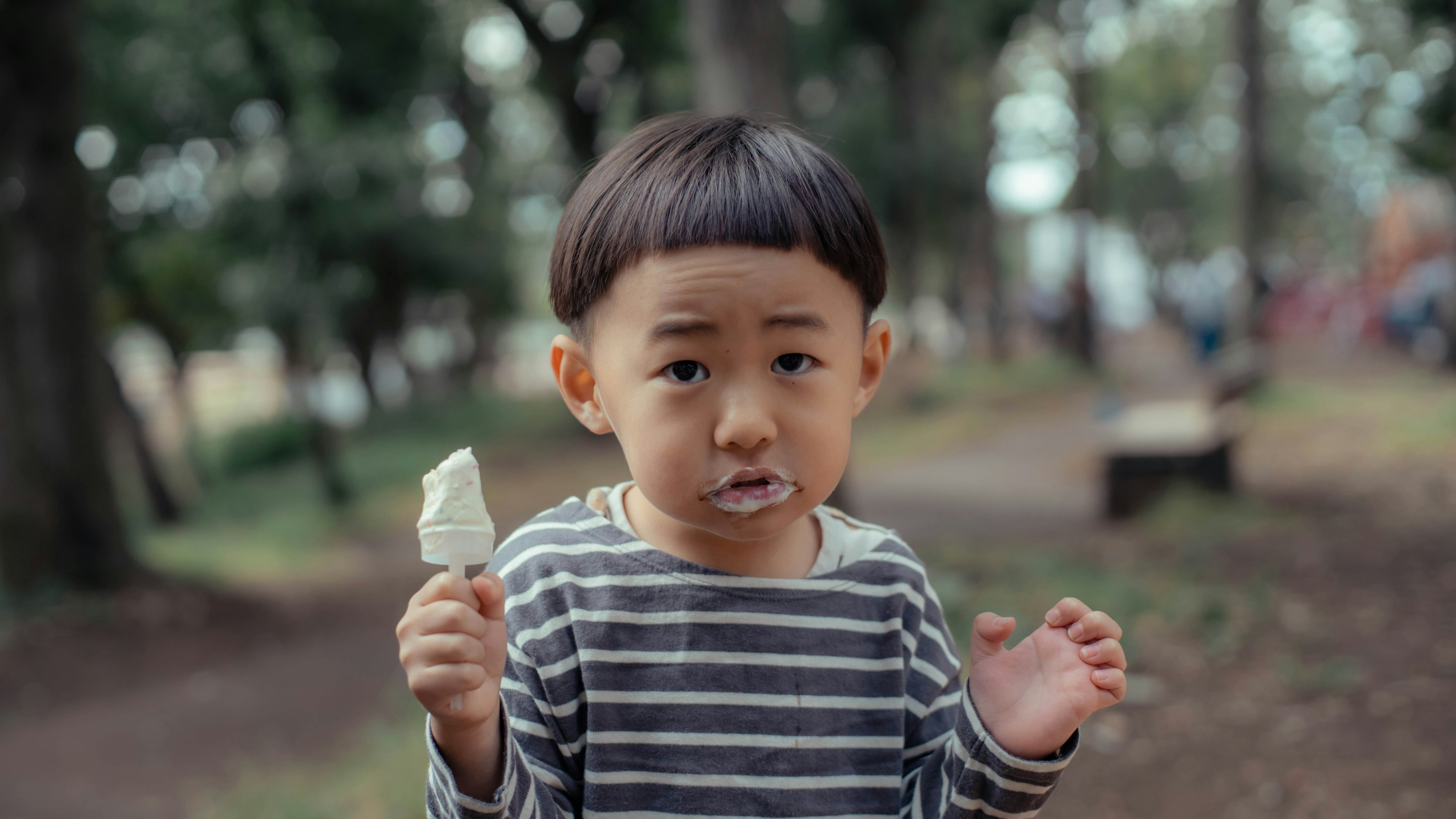 Child holding ice cream in a park with a surprised expression