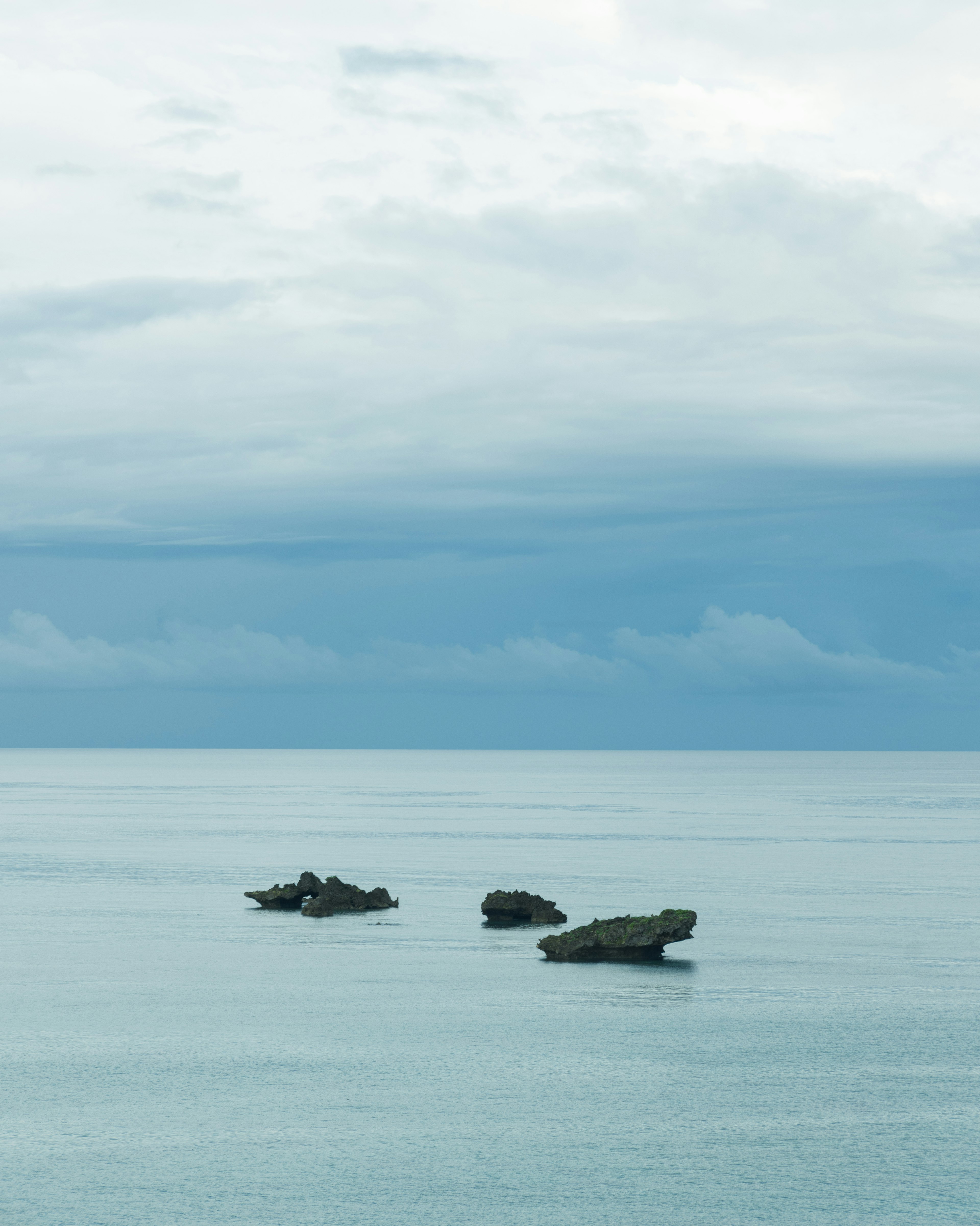 Tres rocas flotando en un mar tranquilo con un cielo nublado