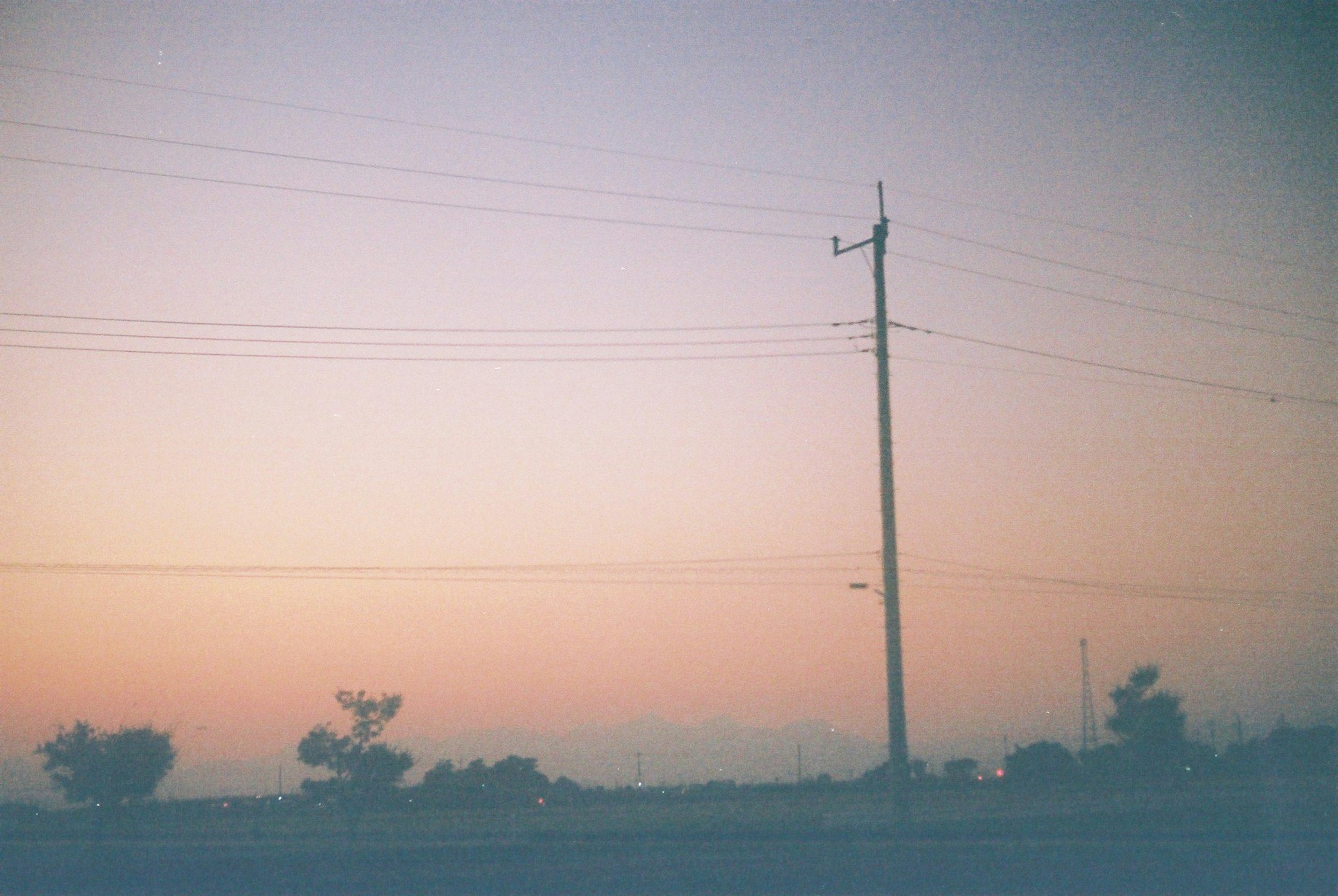 Cielo crepuscular con un poste de luz y siluetas de árboles