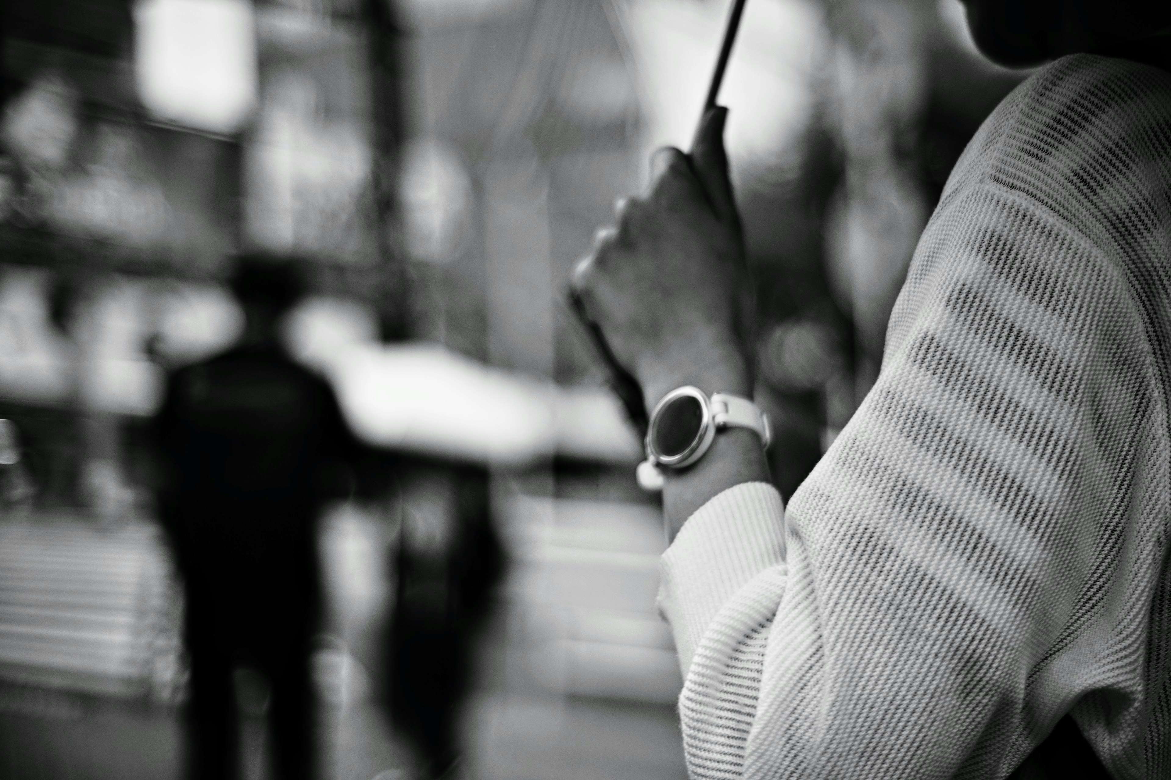 A person's hand holding an umbrella with a watch visible in a black and white city scene