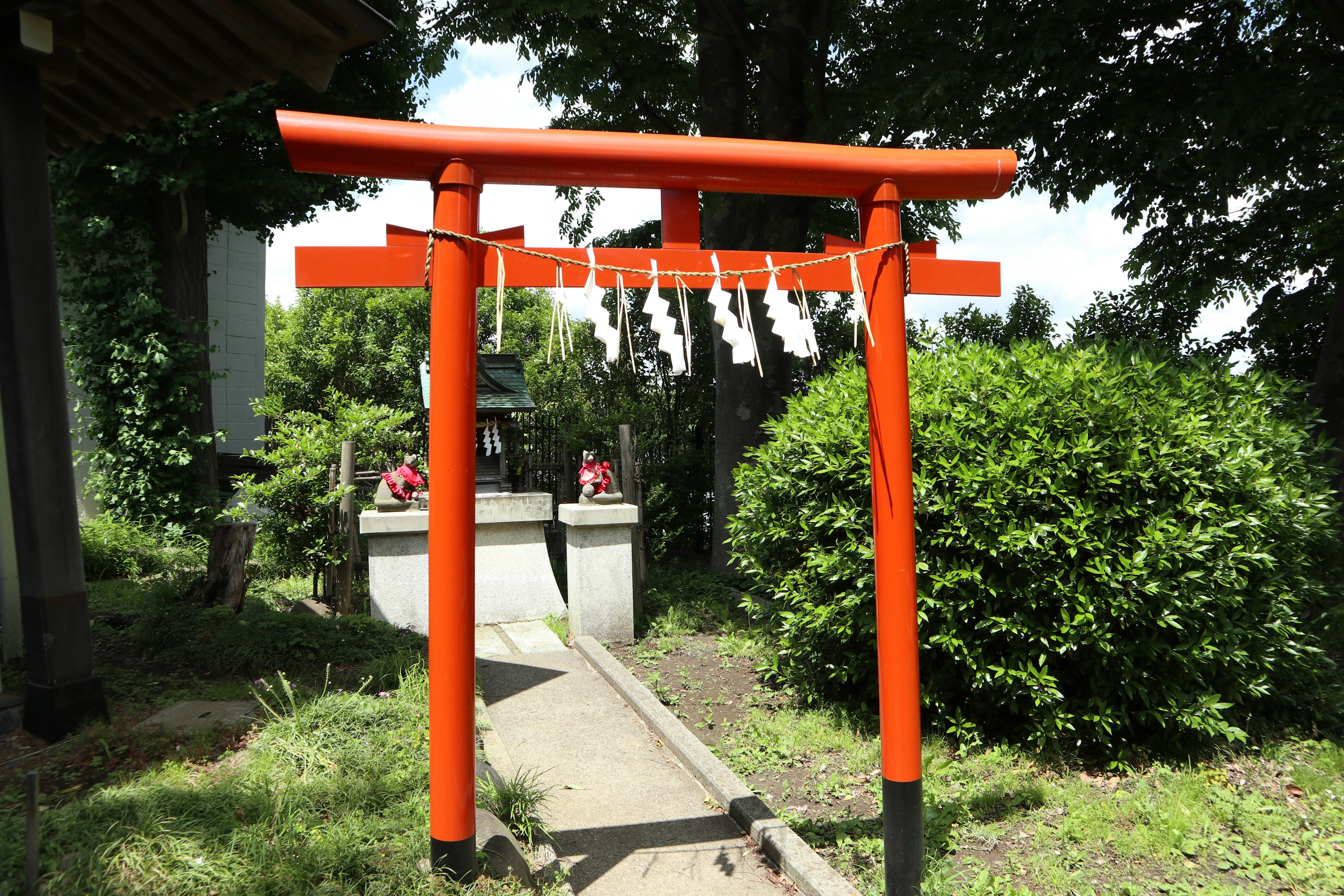 Blick auf ein rotes Torii an einem Schrein-Eingang umgeben von Grün