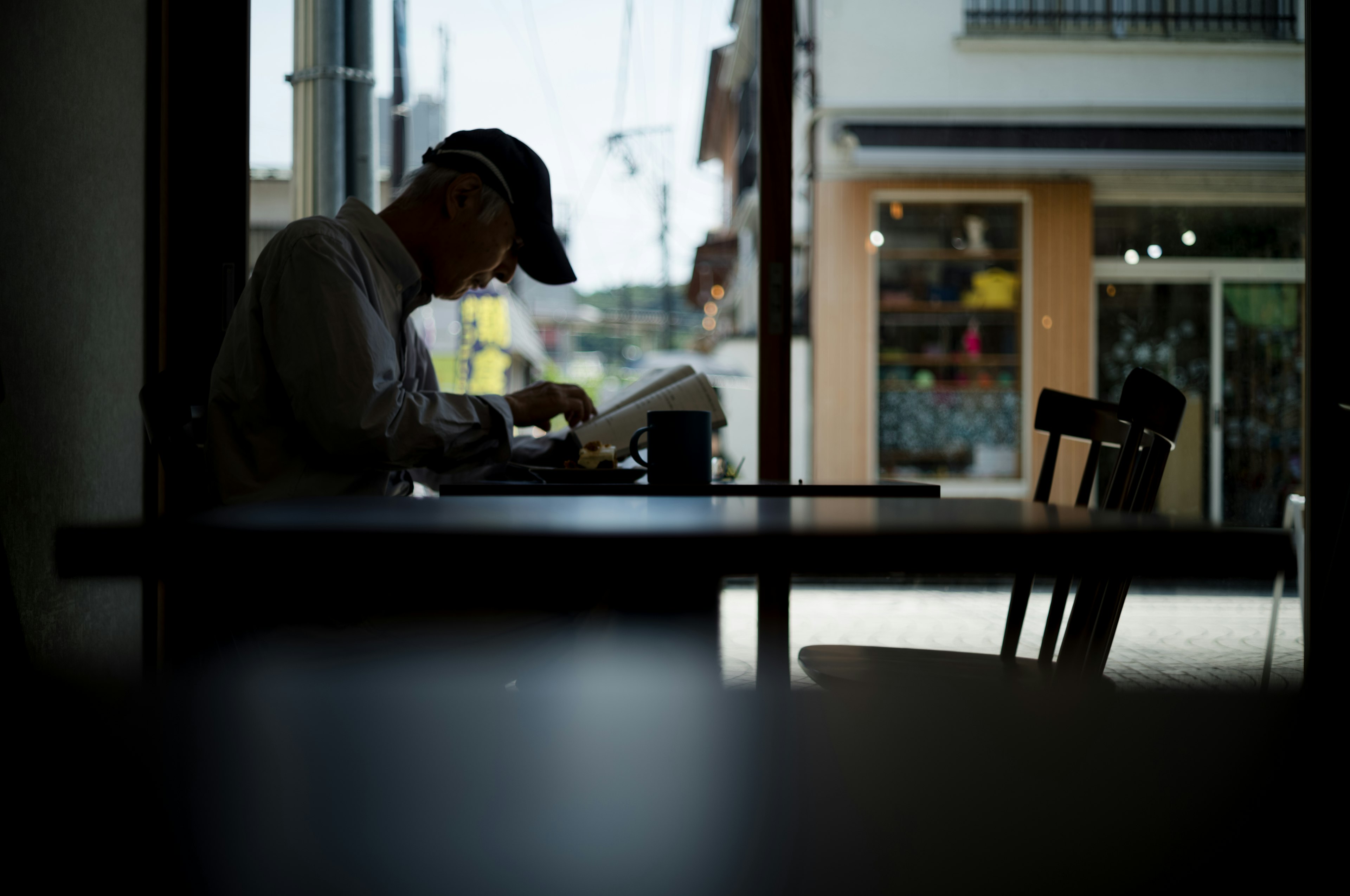 Silhouette eines Mannes, der in einem Café ein Buch liest mit Blick nach draußen