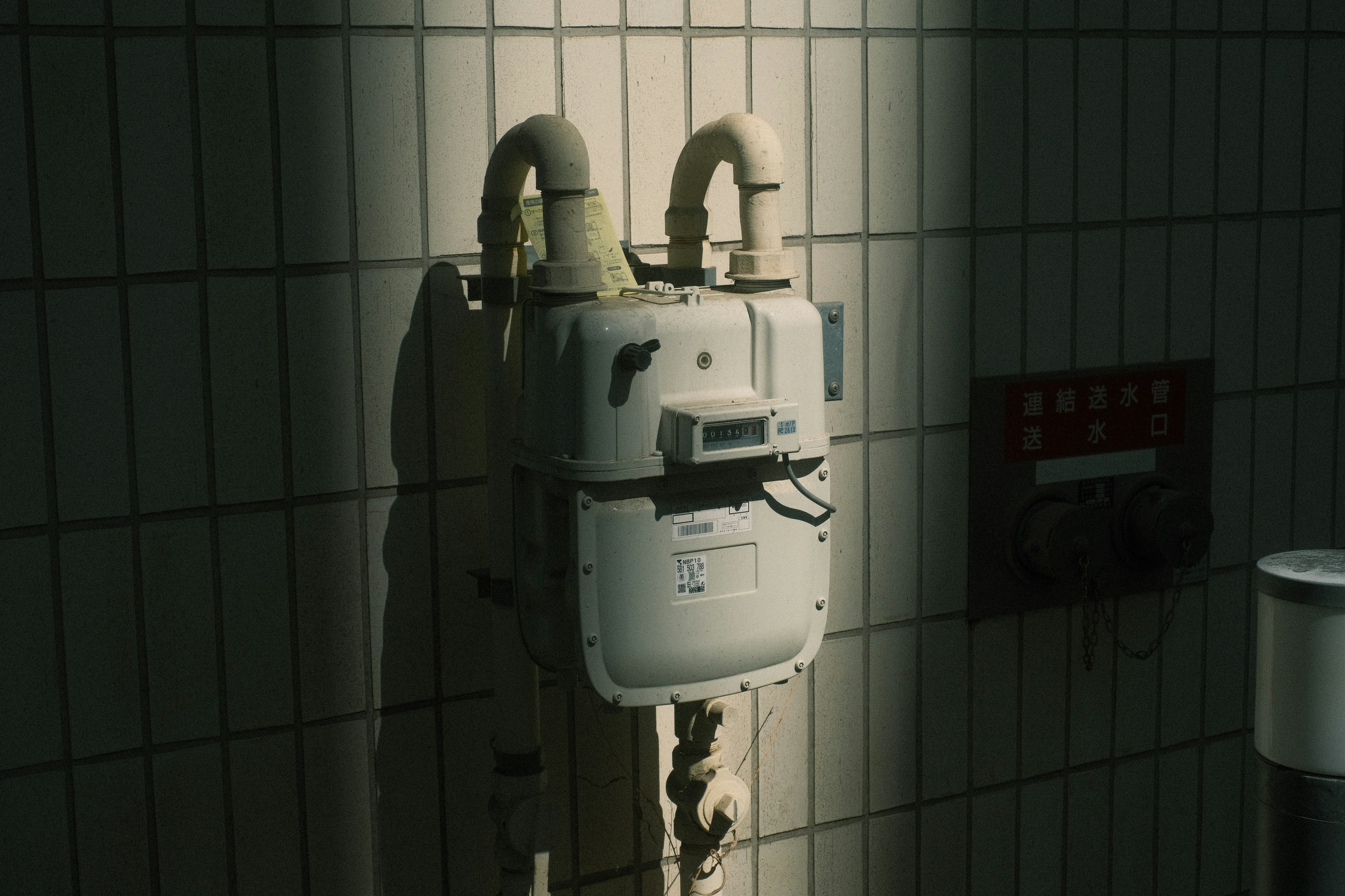 Contador de agua blanco montado en una pared de azulejos con sombras